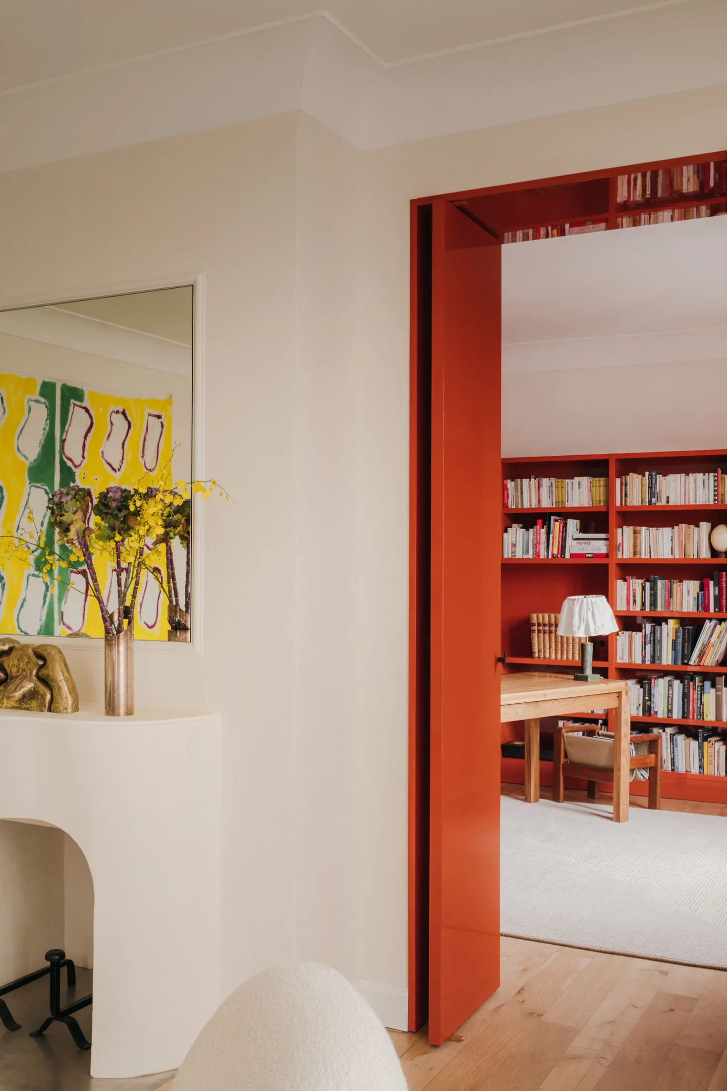 Modern home office with red-painted wooden door and yellow-green abstract artwork hanging on white wall.