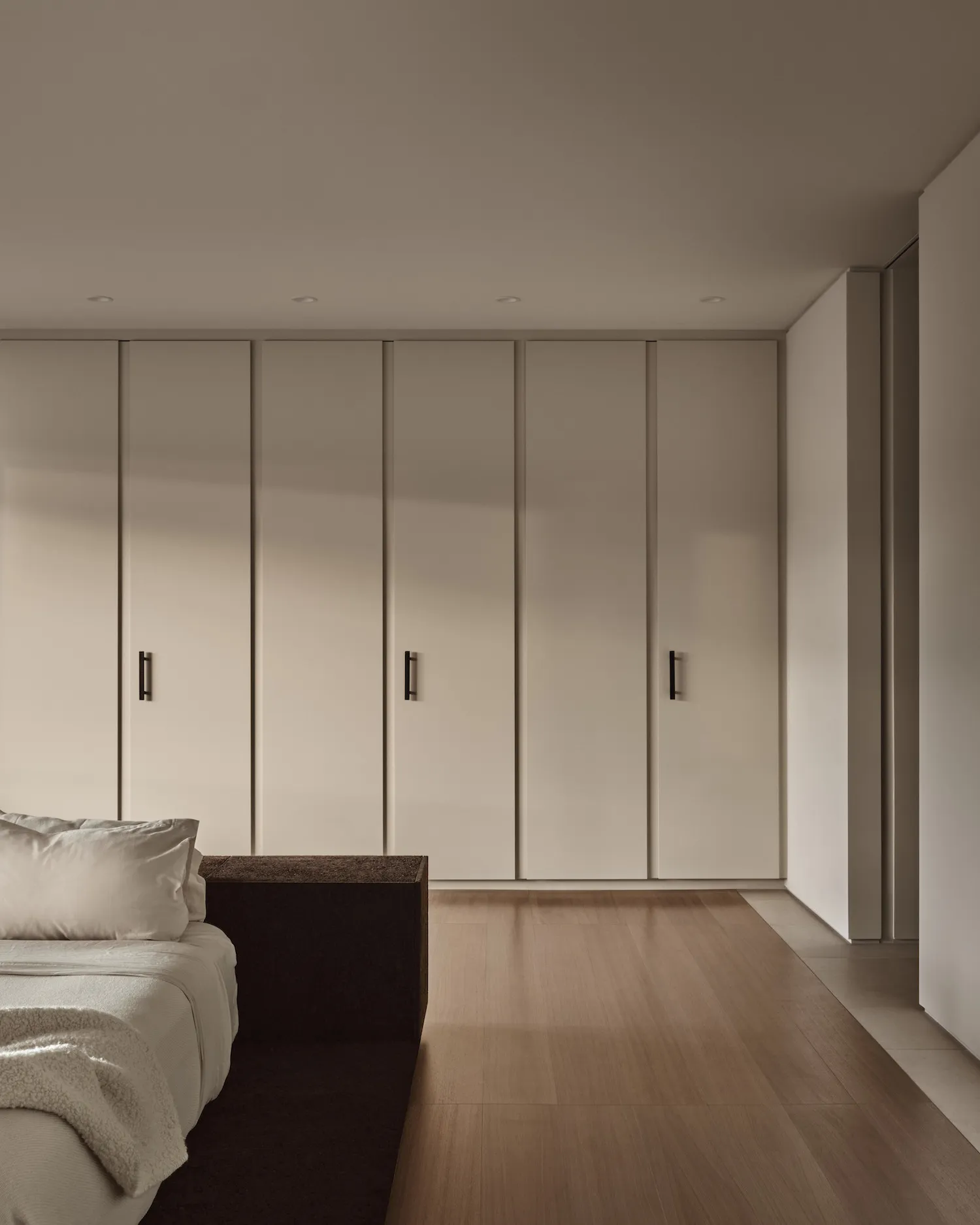 A minimalist bedroom featuring white paneling and wooden floors, with a sleek bed and minimalistic decor.