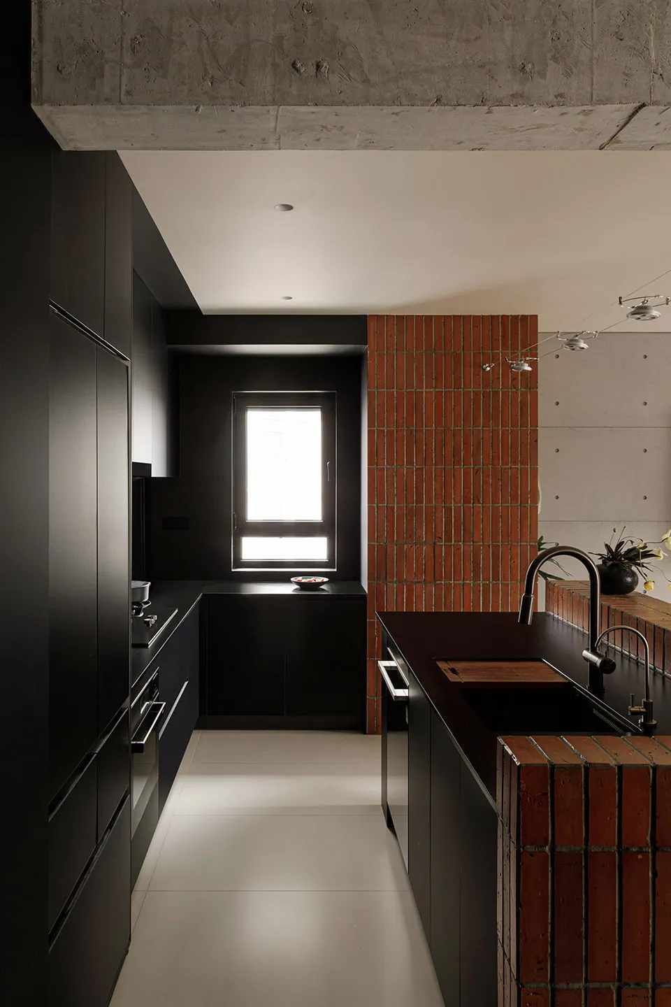 Modern residential kitchen with black cabinets, brick accent wall, and concrete ceiling.