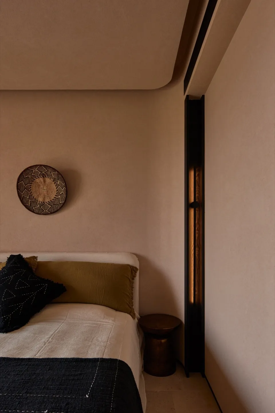 Minimalist bedroom with a bed, bedside stool, and decorative basket on the wall.