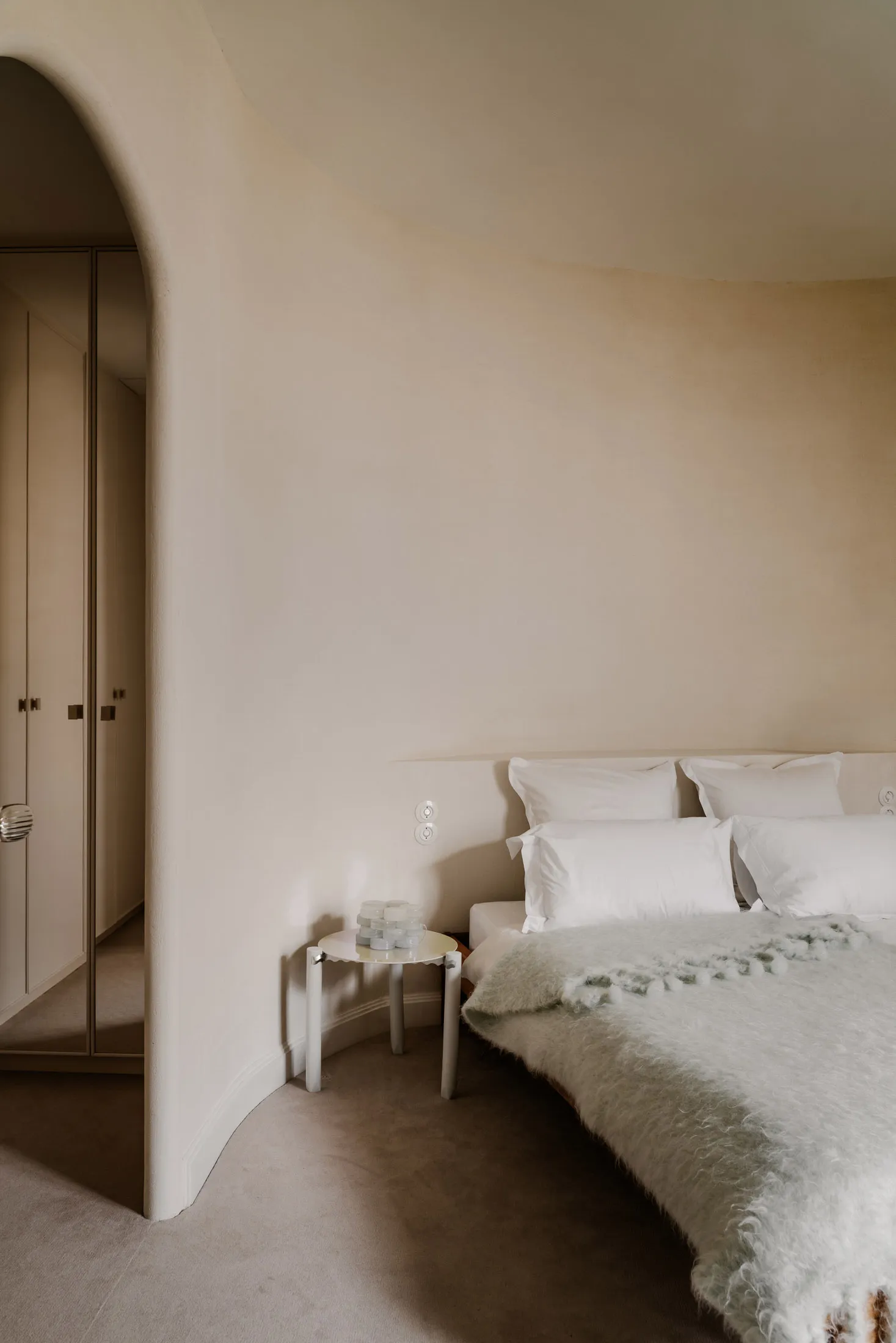 A minimalist bedroom with neutral-toned walls, fabrics, and soft lighting.