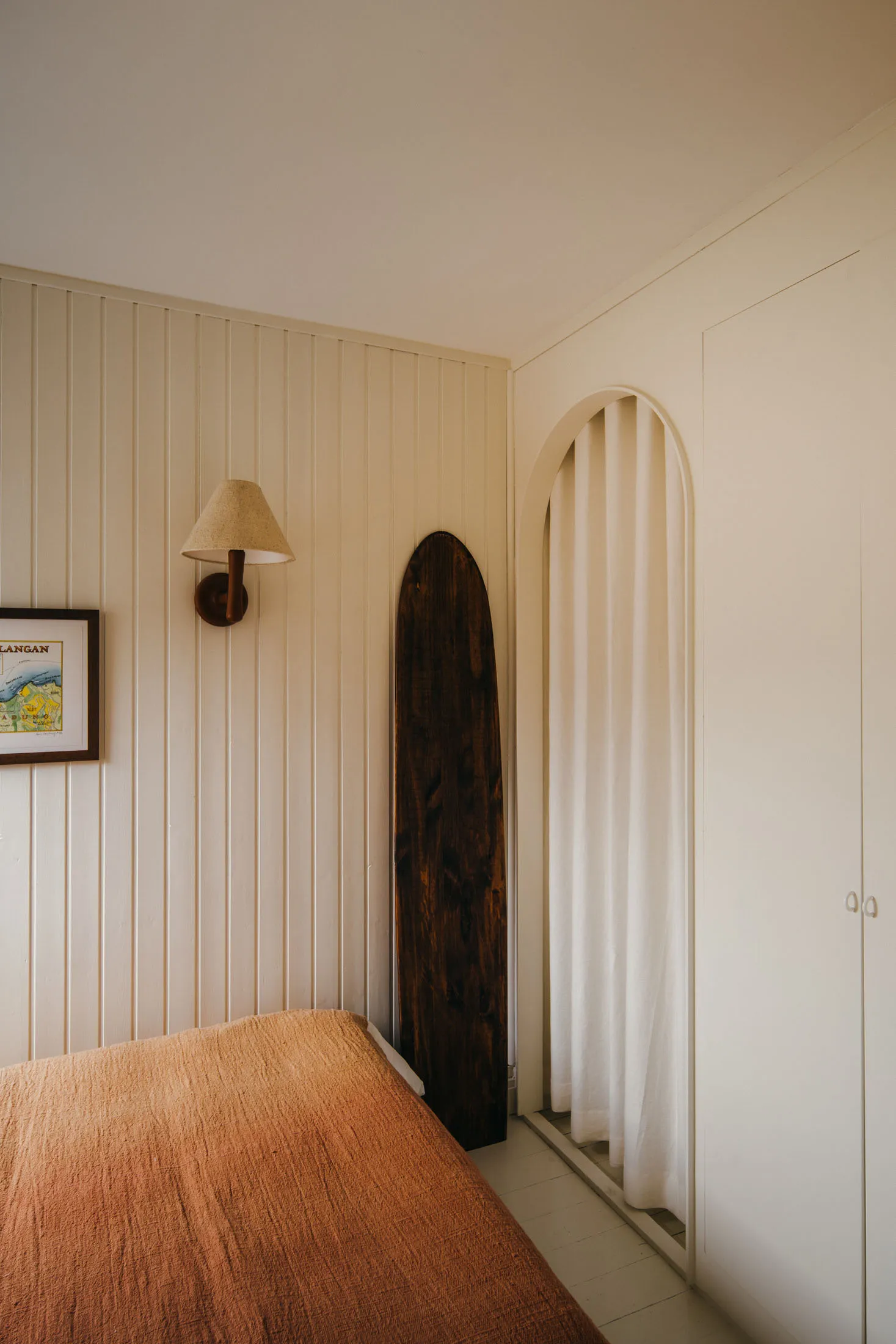 A minimalist bedroom featuring a wooden board and a bed with an orange blanket.