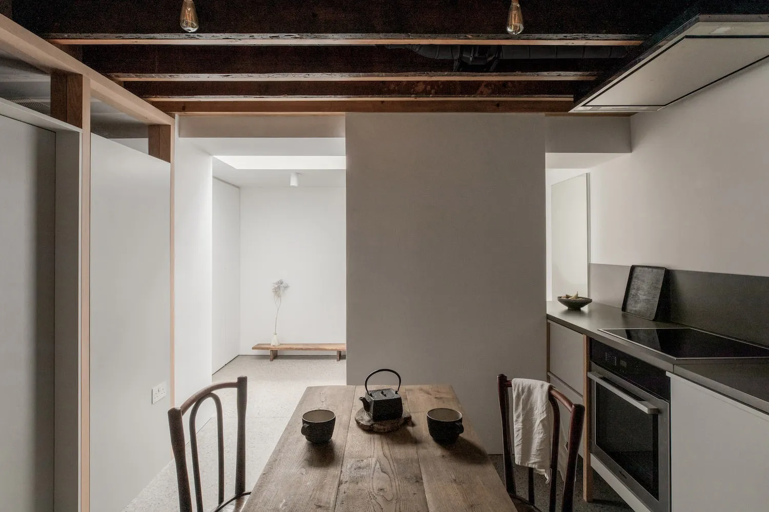 A minimalist residential kitchen with wooden table, concrete walls, and metal accents.