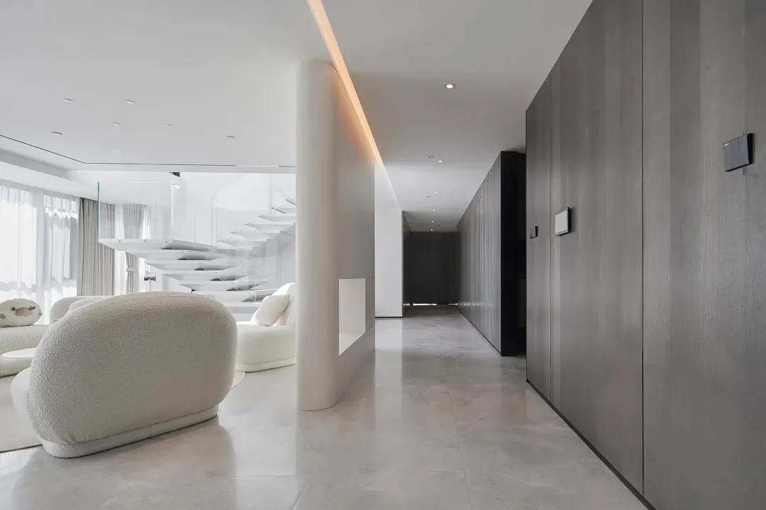 Modern living room with marble floating staircase and black wood cabinets on white marble floor.