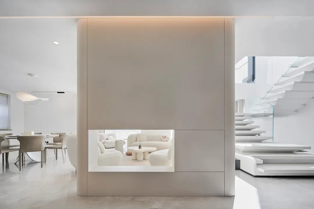 Modern minimalist living room with concrete walls, white furniture, and a glass spiral staircase.
