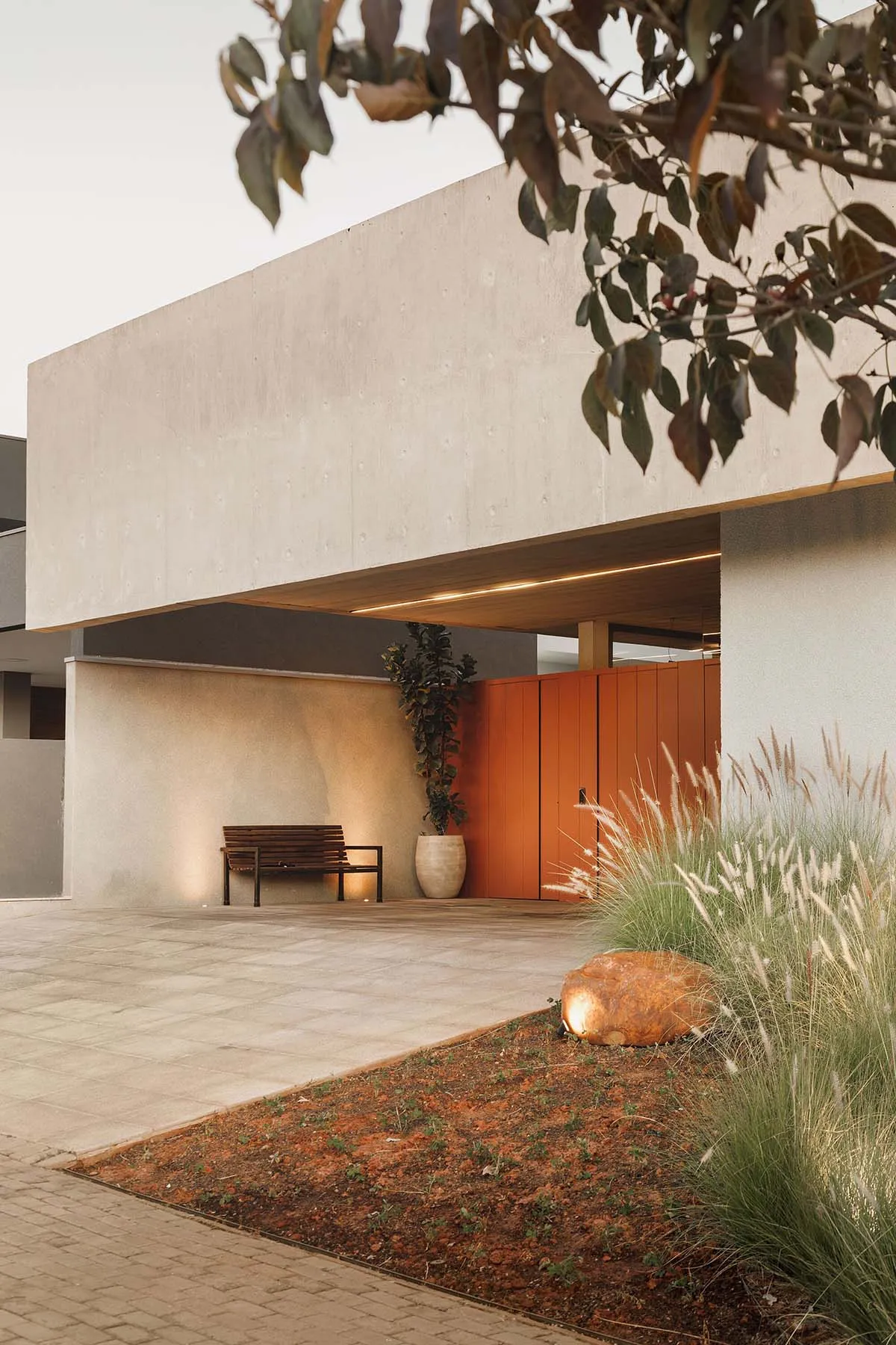 Concrete driveway with bench, potted plant, and garden in front of a modern house.