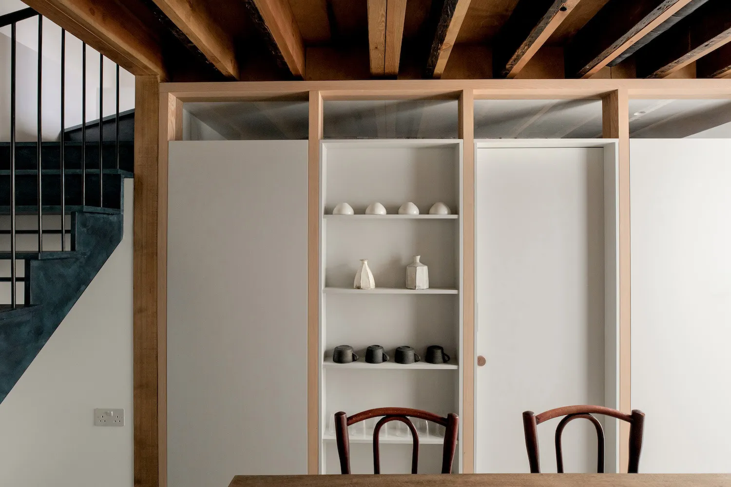 Modern kitchen featuring wooden shelves and minimalist chairs, designed for functionality and style.