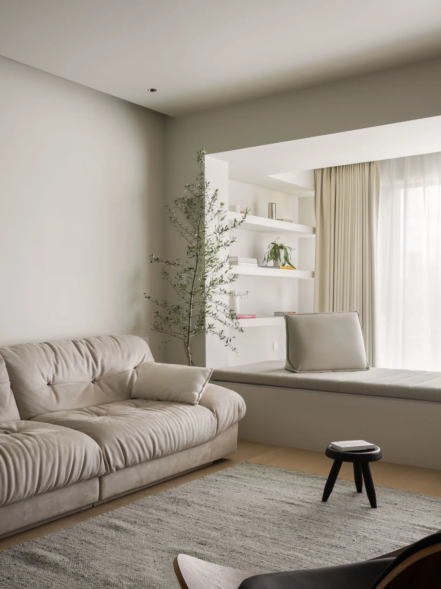 Minimalist living room with neutral-colored furniture, a large window, and a small stool.