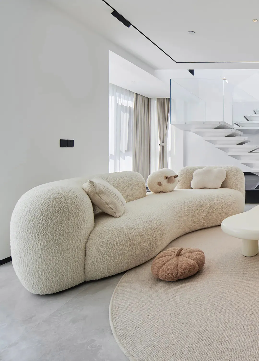 A modern living room with a textured sofa, round ottoman, and minimalistic design.