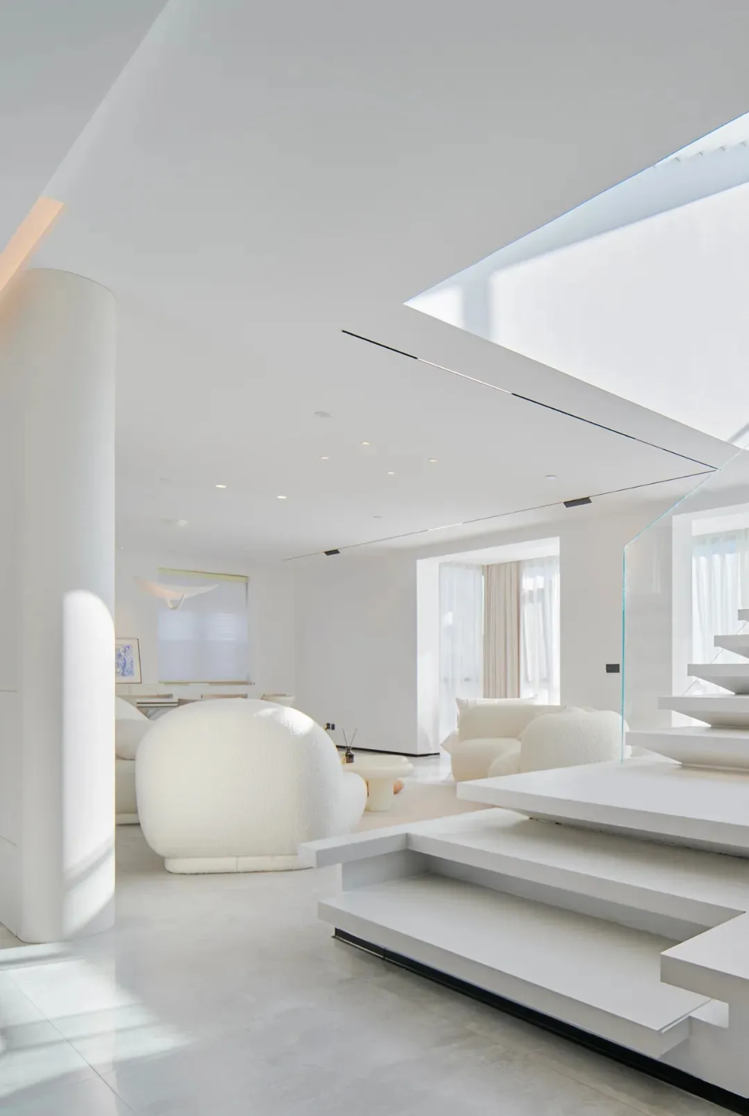 A modern, white living room with glass walls and a white sofa.