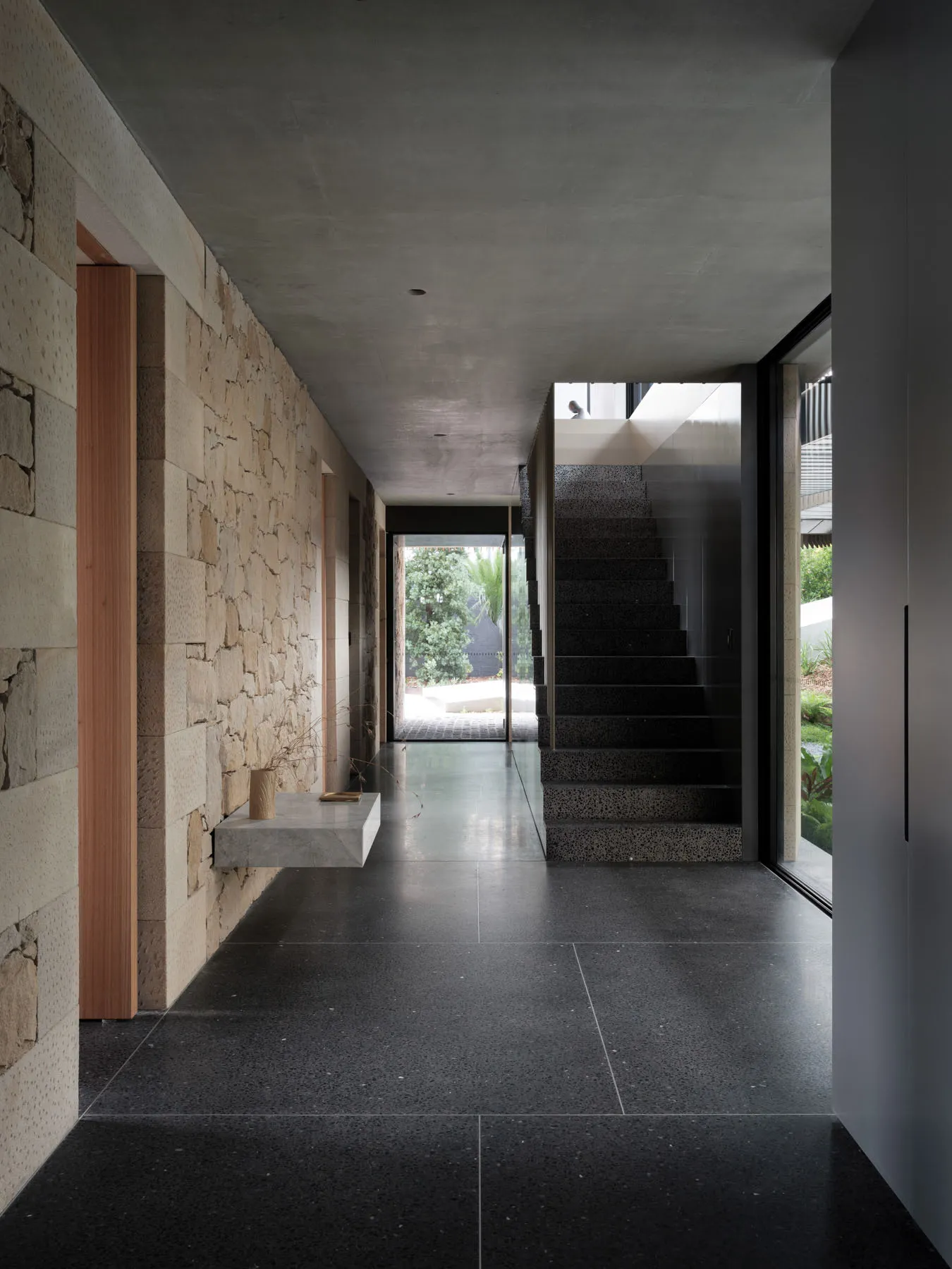 A modern entryway featuring concrete flooring, a stone wall, and a glass door.
