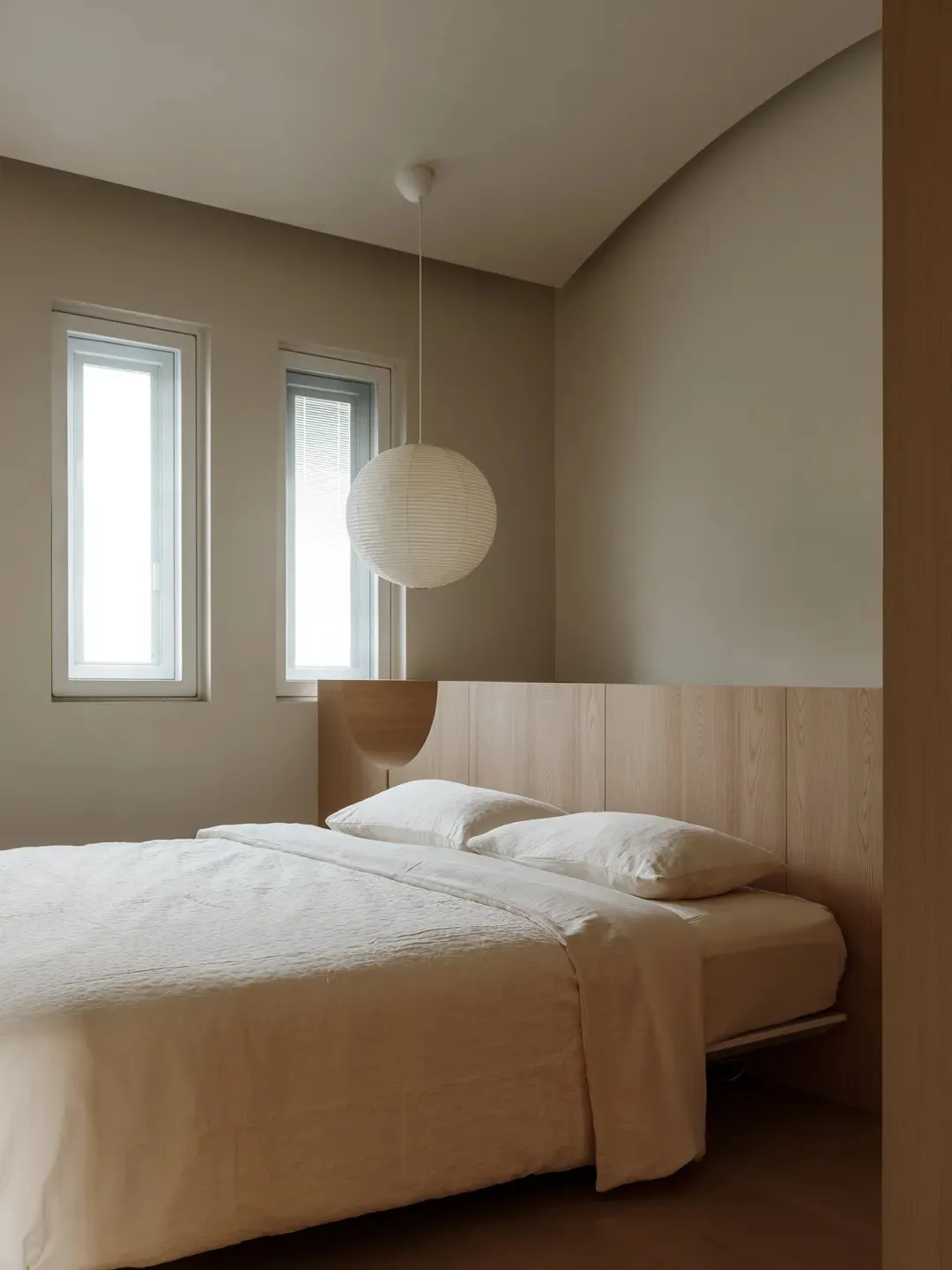 Minimalist bedroom featuring a bed with wood paneling and a spherical lamp hanging from the ceiling.