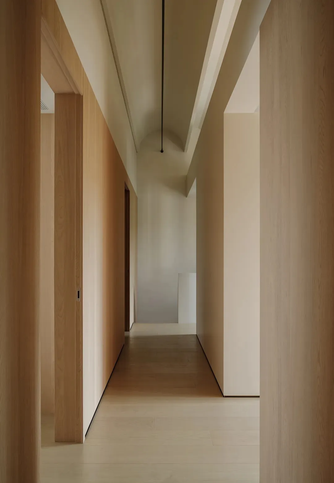 A minimalist corridor with wooden walls and floors, arch-shaped ceiling details, and arch-shaped openings for doors.