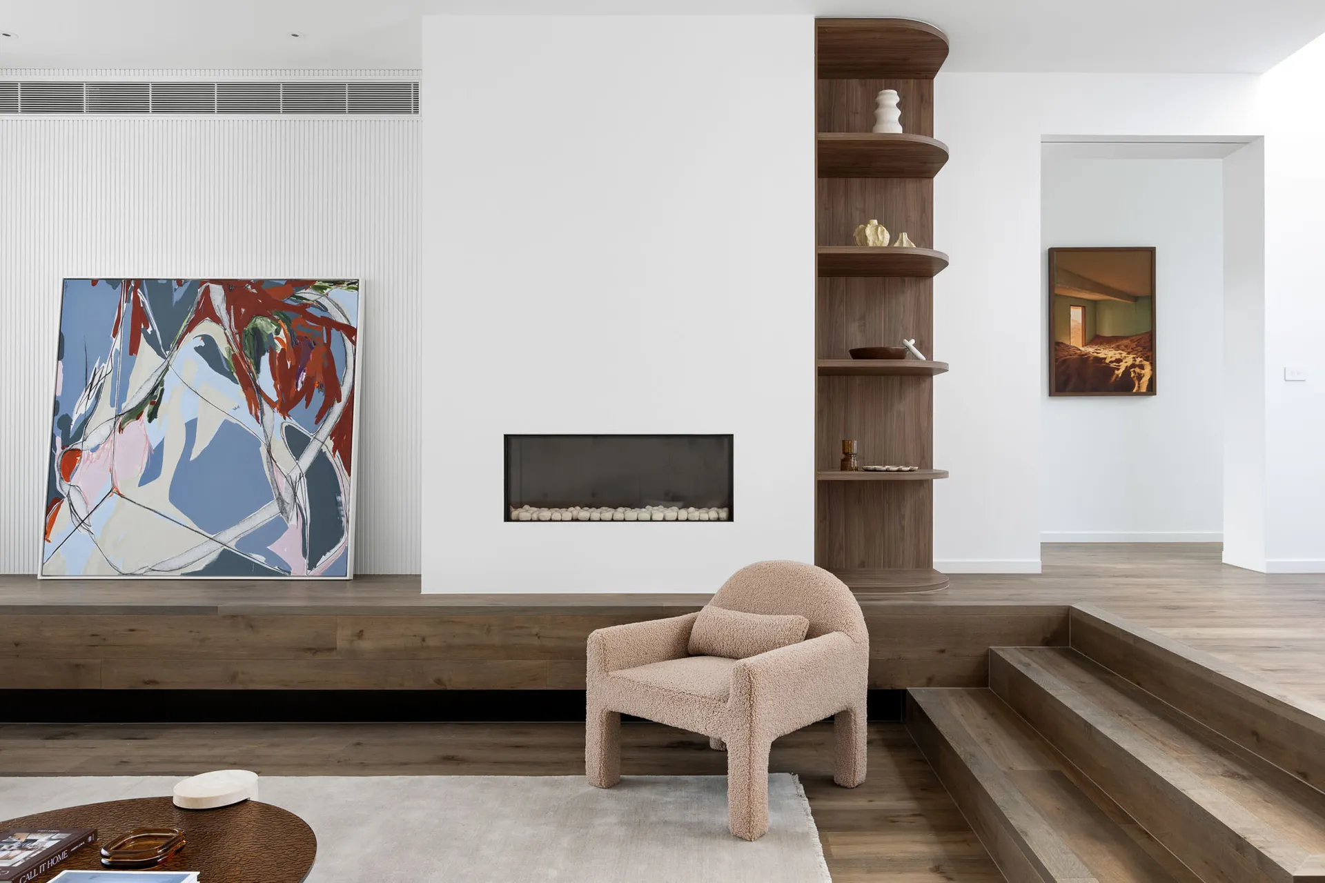A minimalist living room featuring a wooden floor, a modern fireplace, and abstract art on the walls.