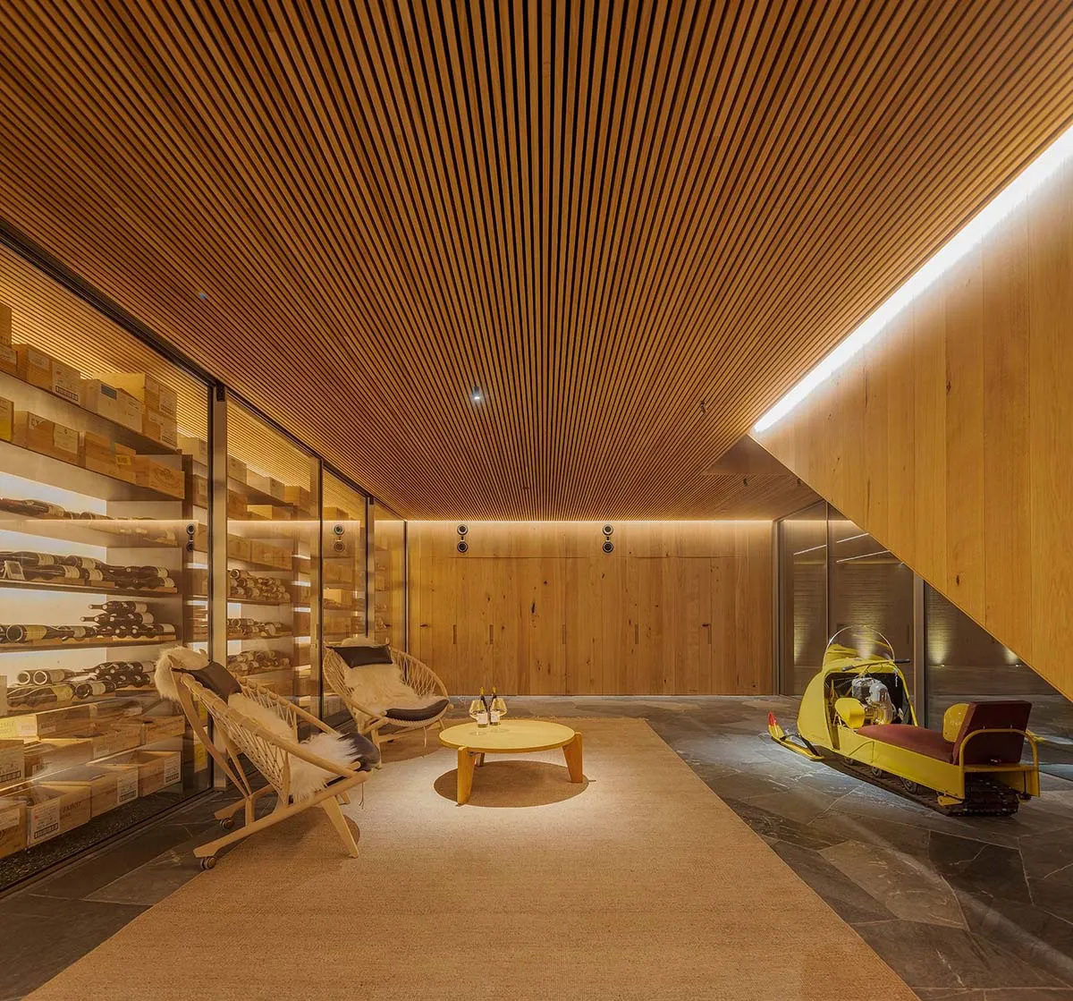 A minimalist wine cellar with wooden walls, featuring shelves filled with bottles of wine and a yellow snowmobile.