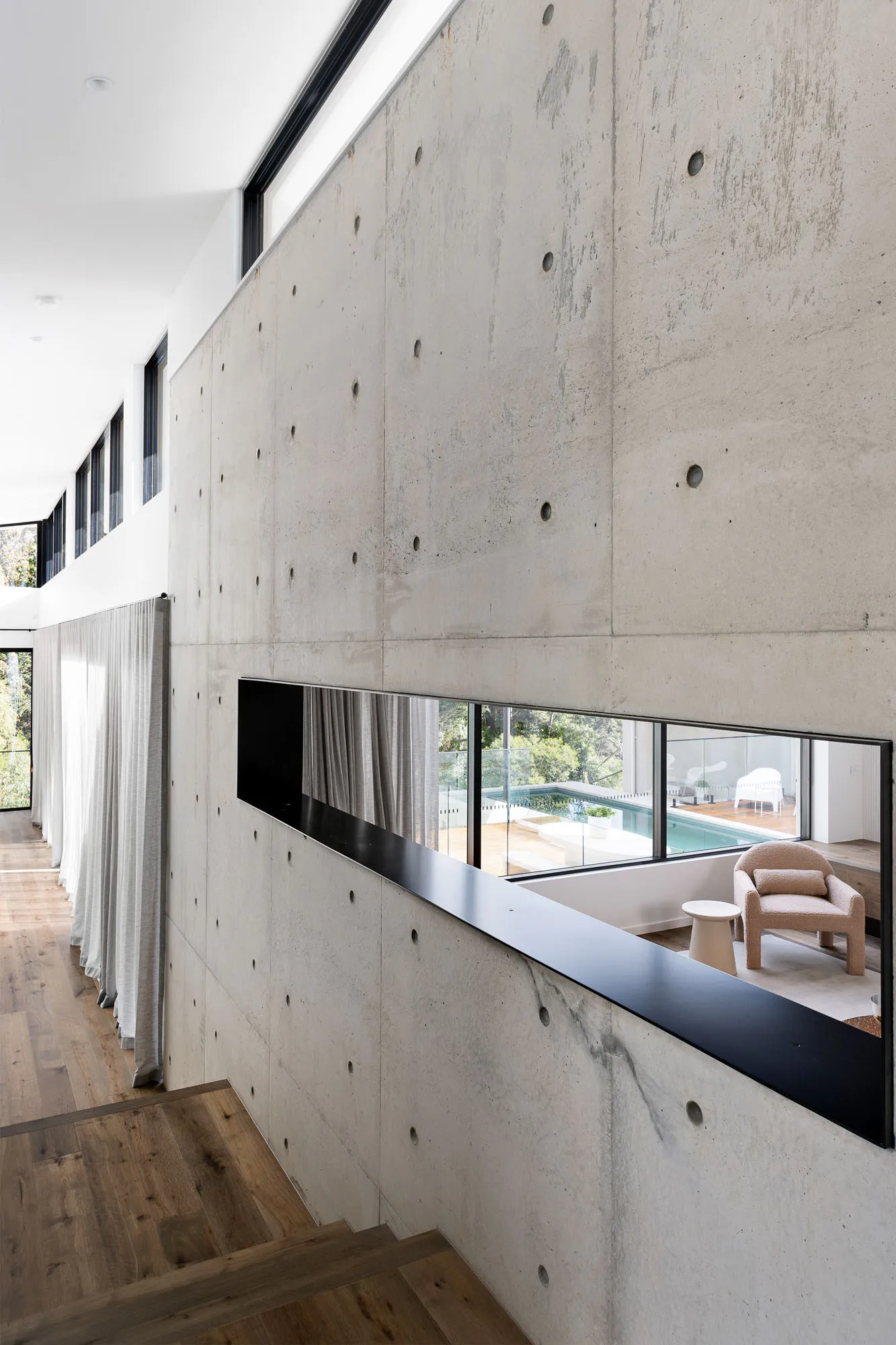 Minimalist living room with concrete walls, featuring a cozy seating area and a view of a swimming pool.