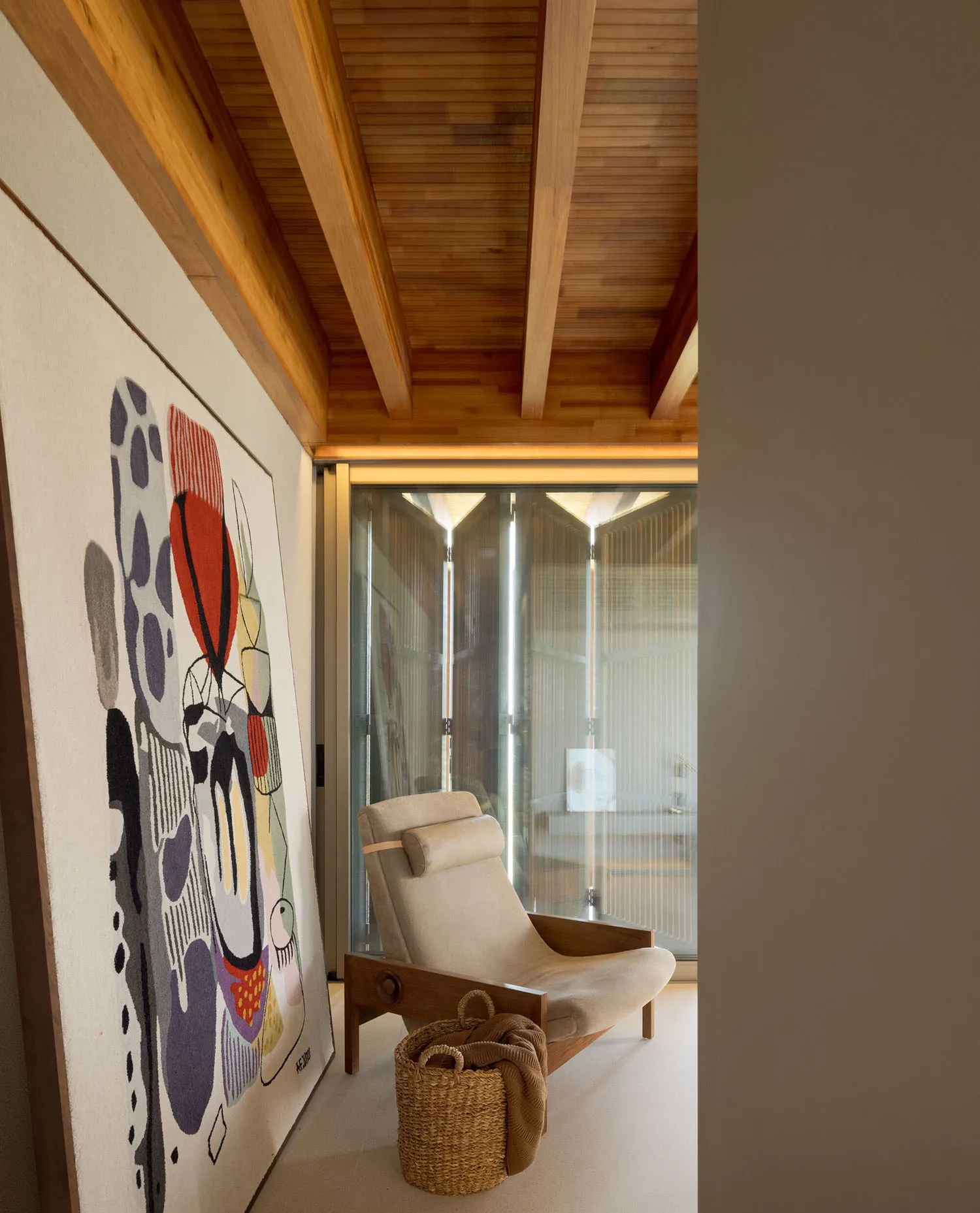 A modern living room featuring a lounge chair, a large abstract artwork, and a woven basket.