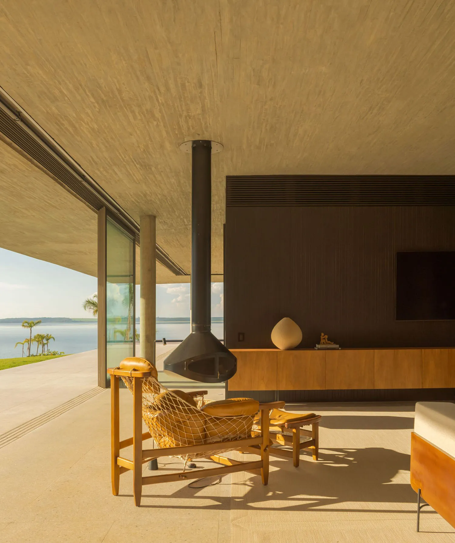 A modern living room with concrete walls and flooring, featuring a hanging fireplace and minimalistic furniture.