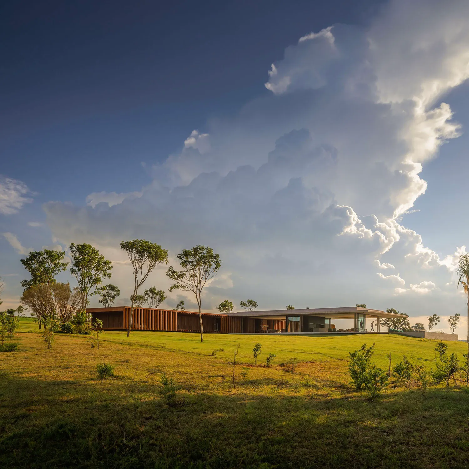 Modern residential house with wood and glass features, set against a backdrop of blue sky and clouds.