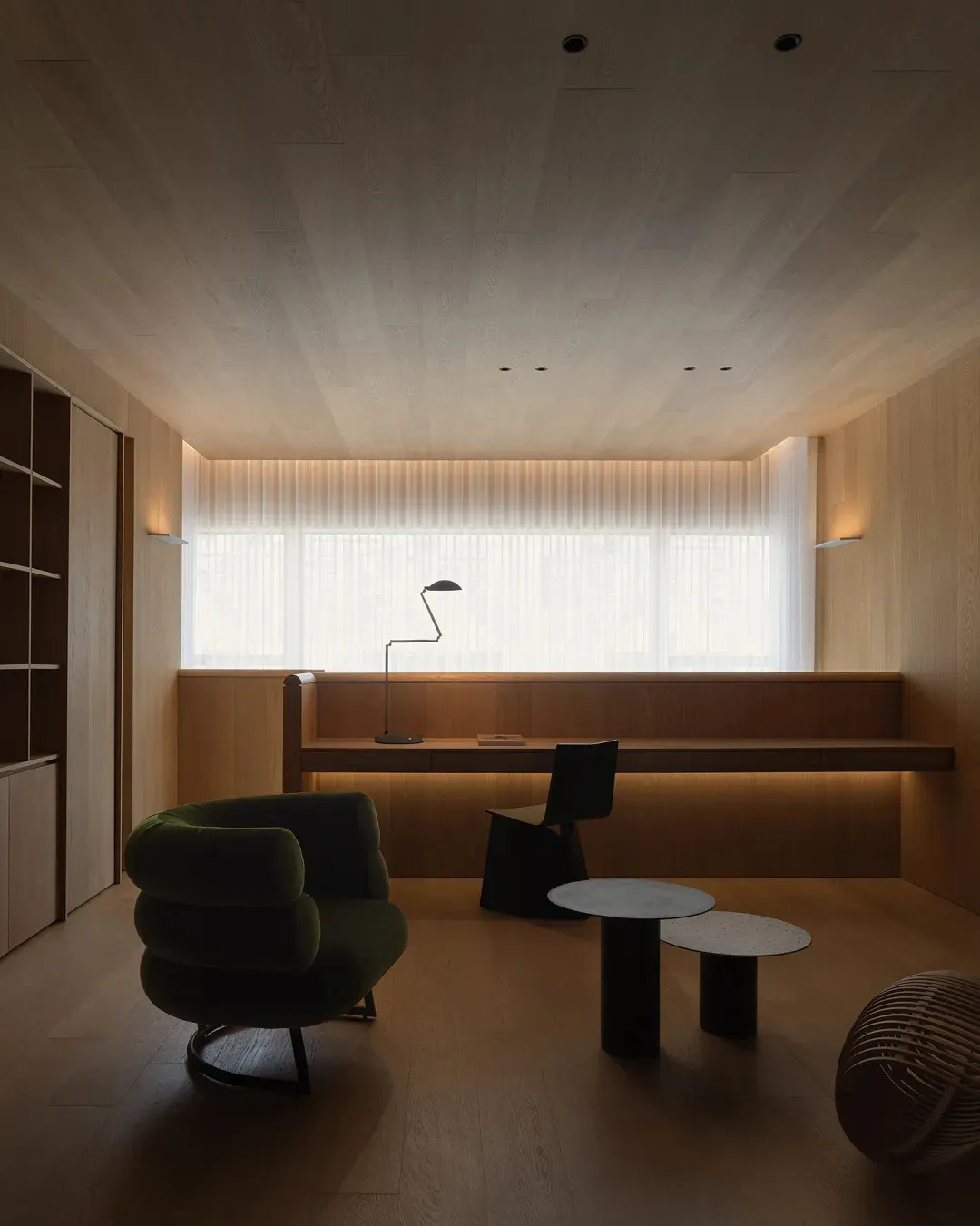 A minimalist living room with wooden elements and a concrete table, featuring a green armchair, a floor lamp, and a long tabl