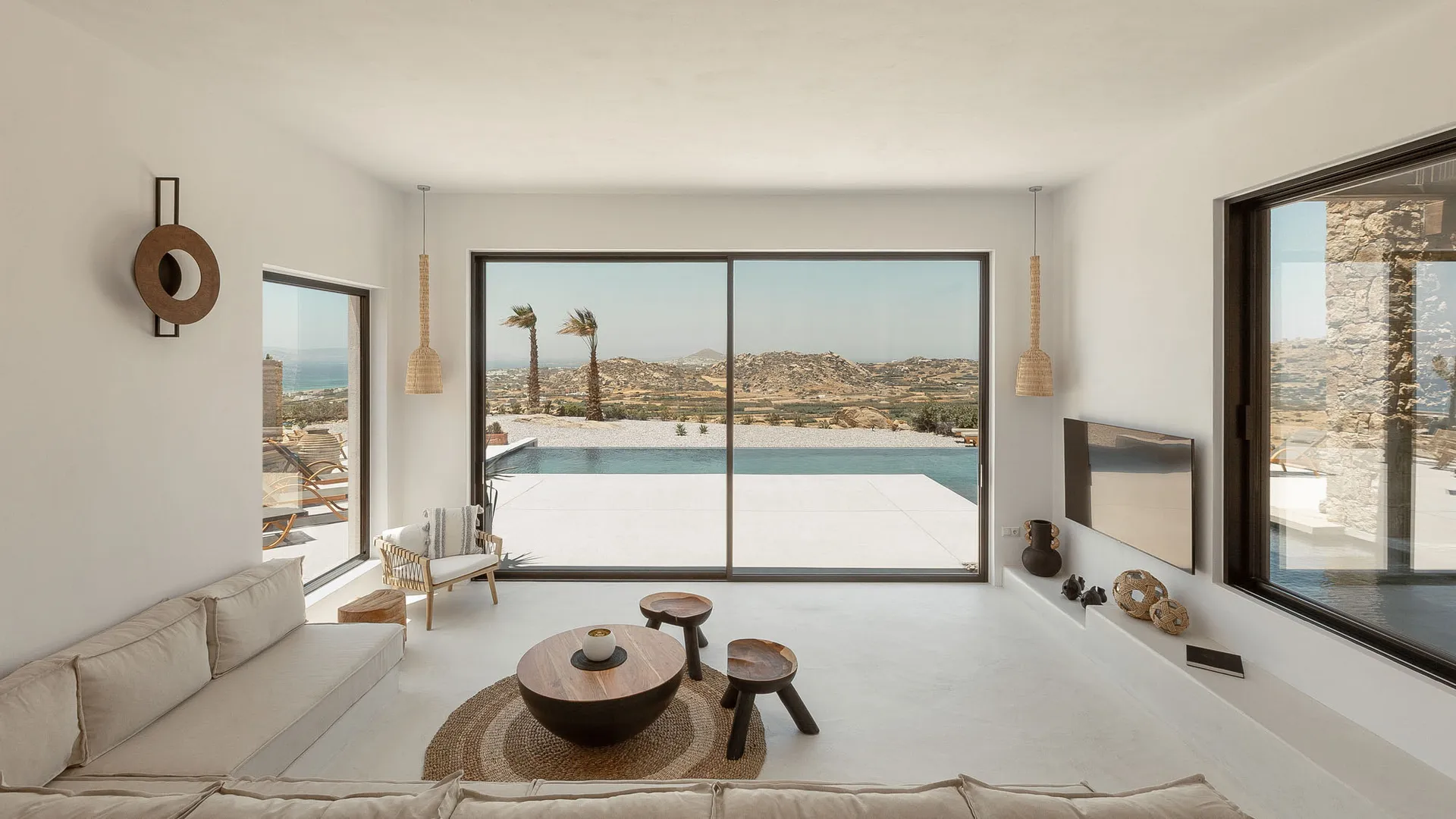 Modern minimalist living room with neutral tones and minimalist decor, overlooking a scenic outdoor area with a pool and natu