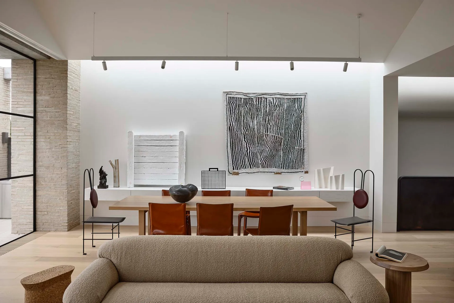 A modern minimalist living room featuring a wooden sofa, leather chairs, and stone elements.