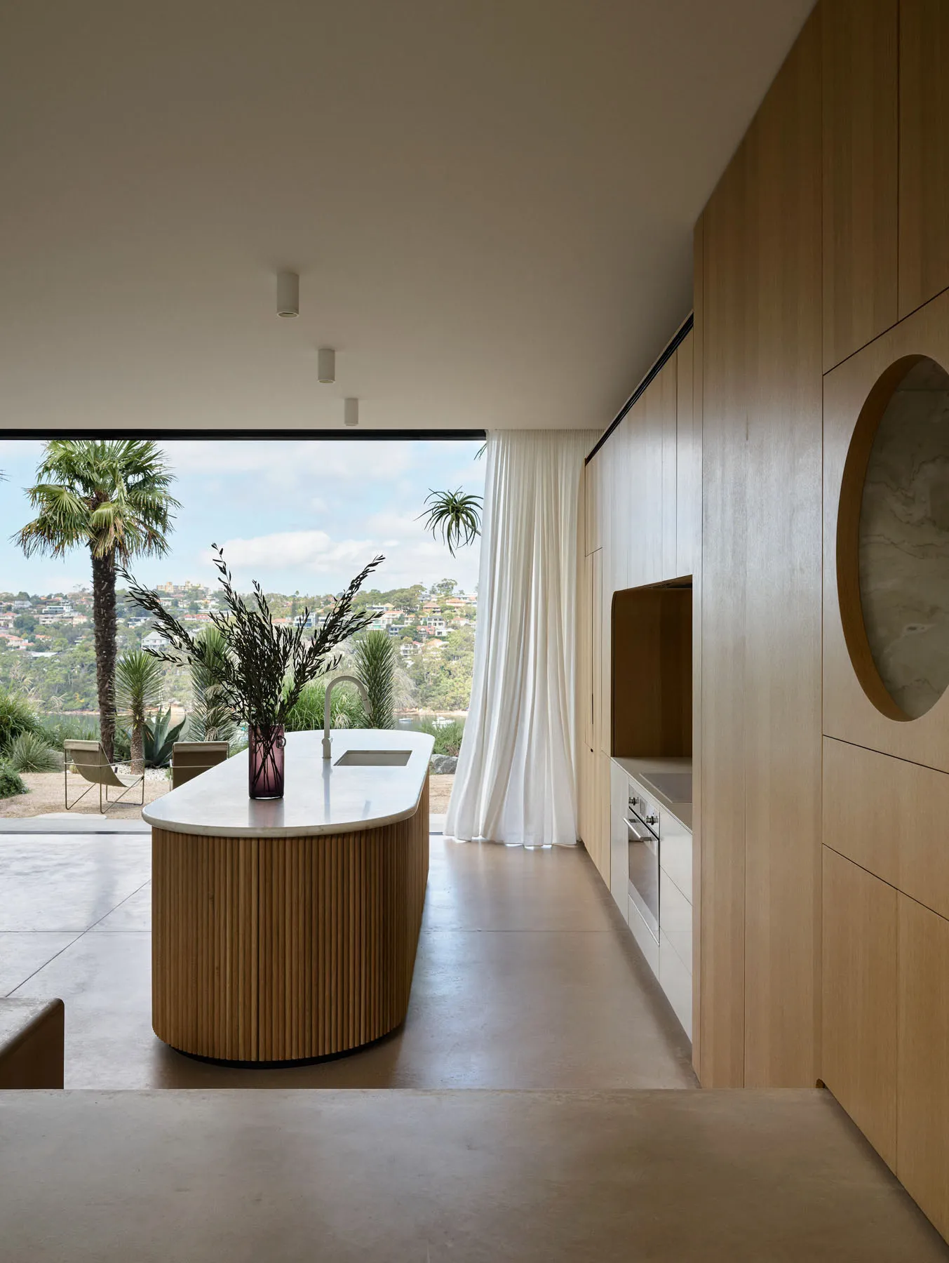 Modern residential interior with a kitchen island made of wood and a concrete countertop, featuring a view of the outdoors wi