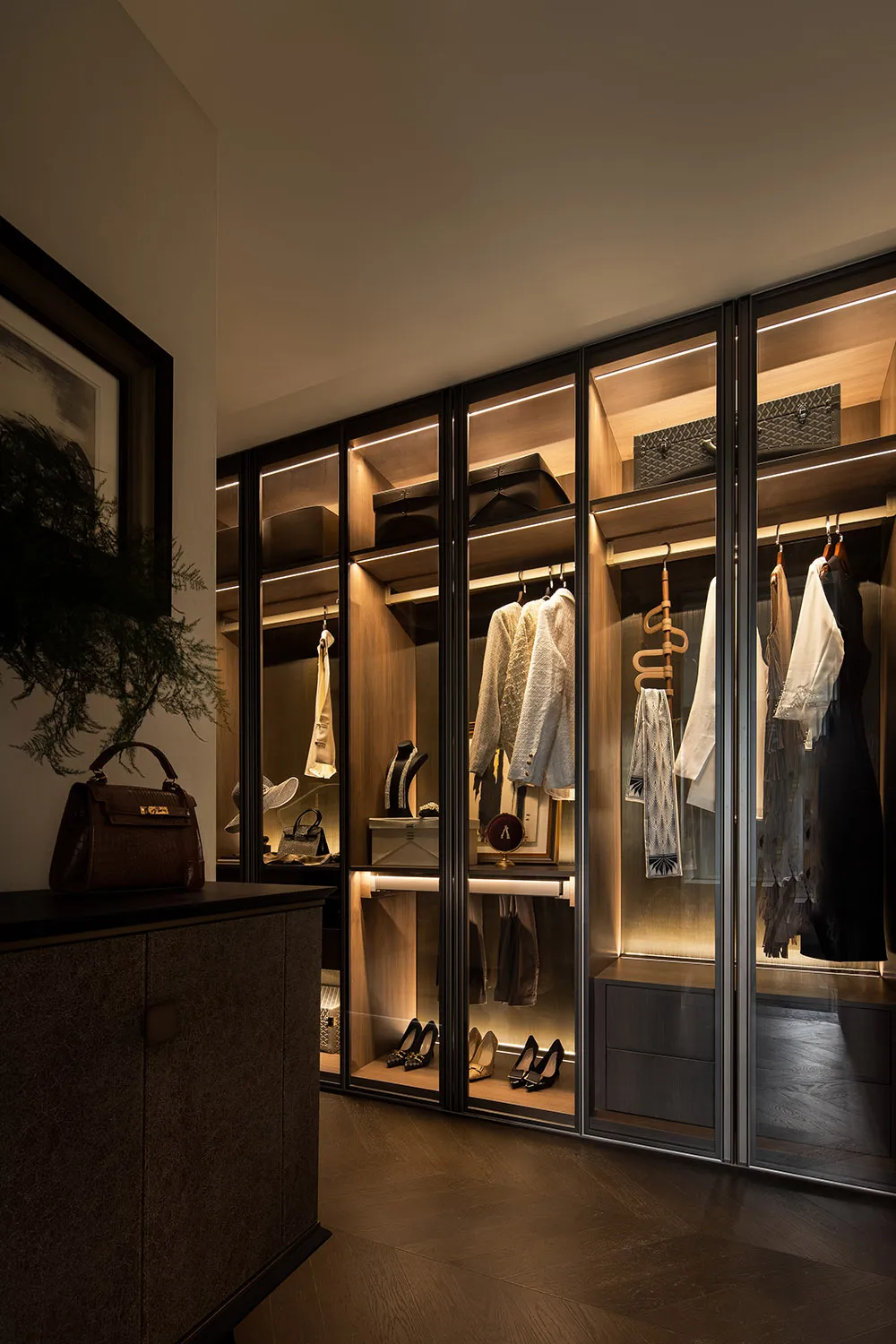 Modern walk-in closet with glass-panel walls, wooden shelving, and metal accents.