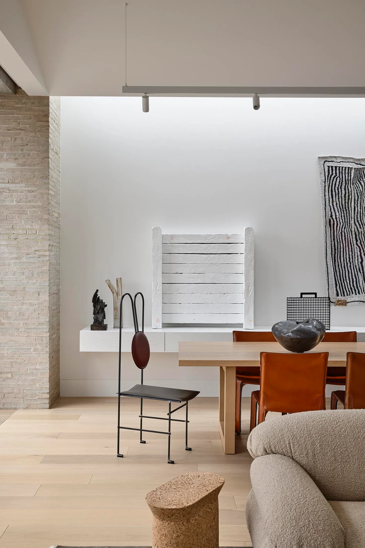 Modern dining room with wooden table, leather chairs, brick wall, and minimalist decor.