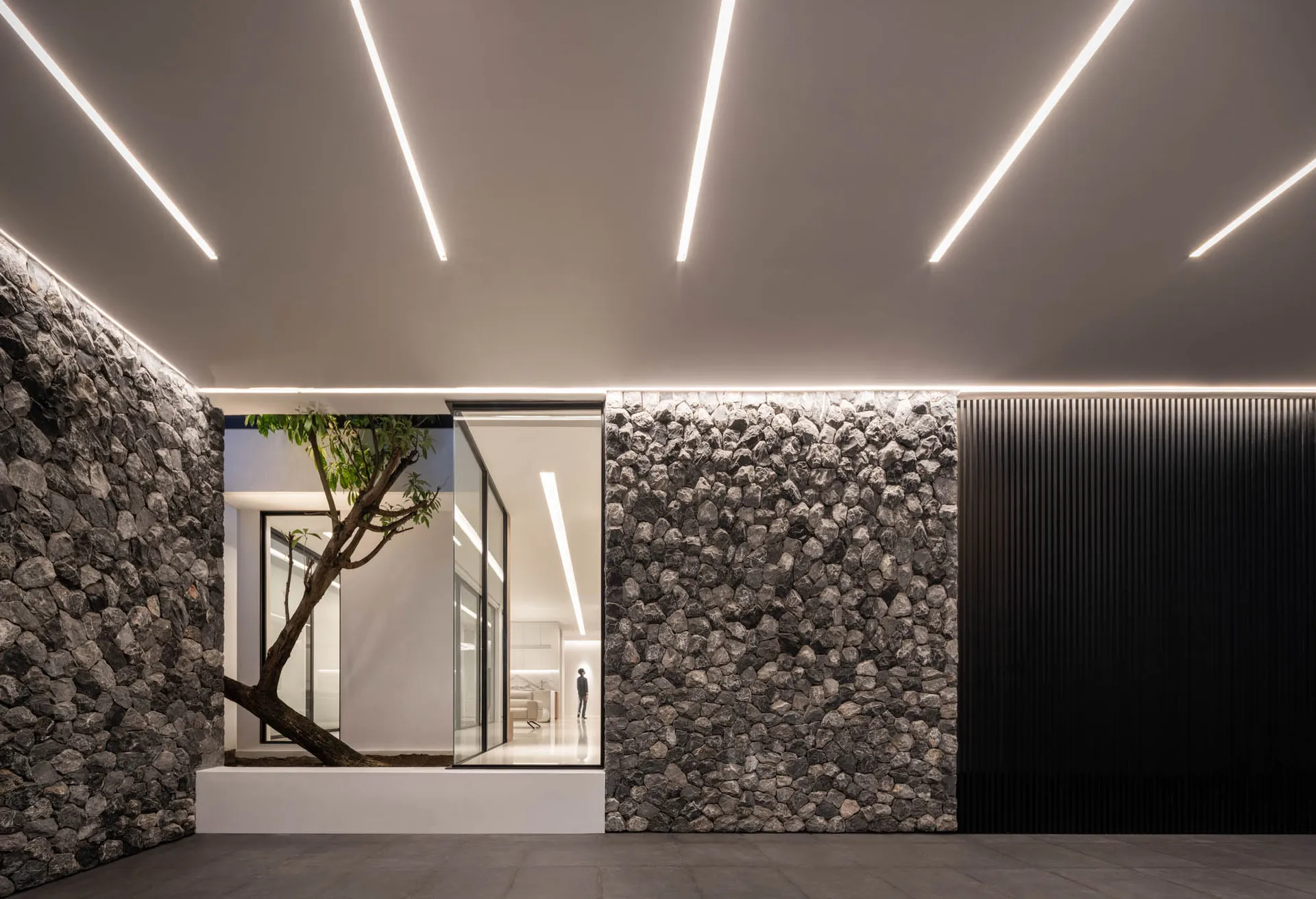 Modern living room with concrete walls and floor, featuring a tree and sleek furniture.