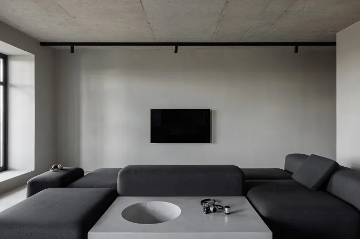 A minimalist living room with a dark gray sofa, a circular coffee table, and a wall-mounted flat-screen TV.