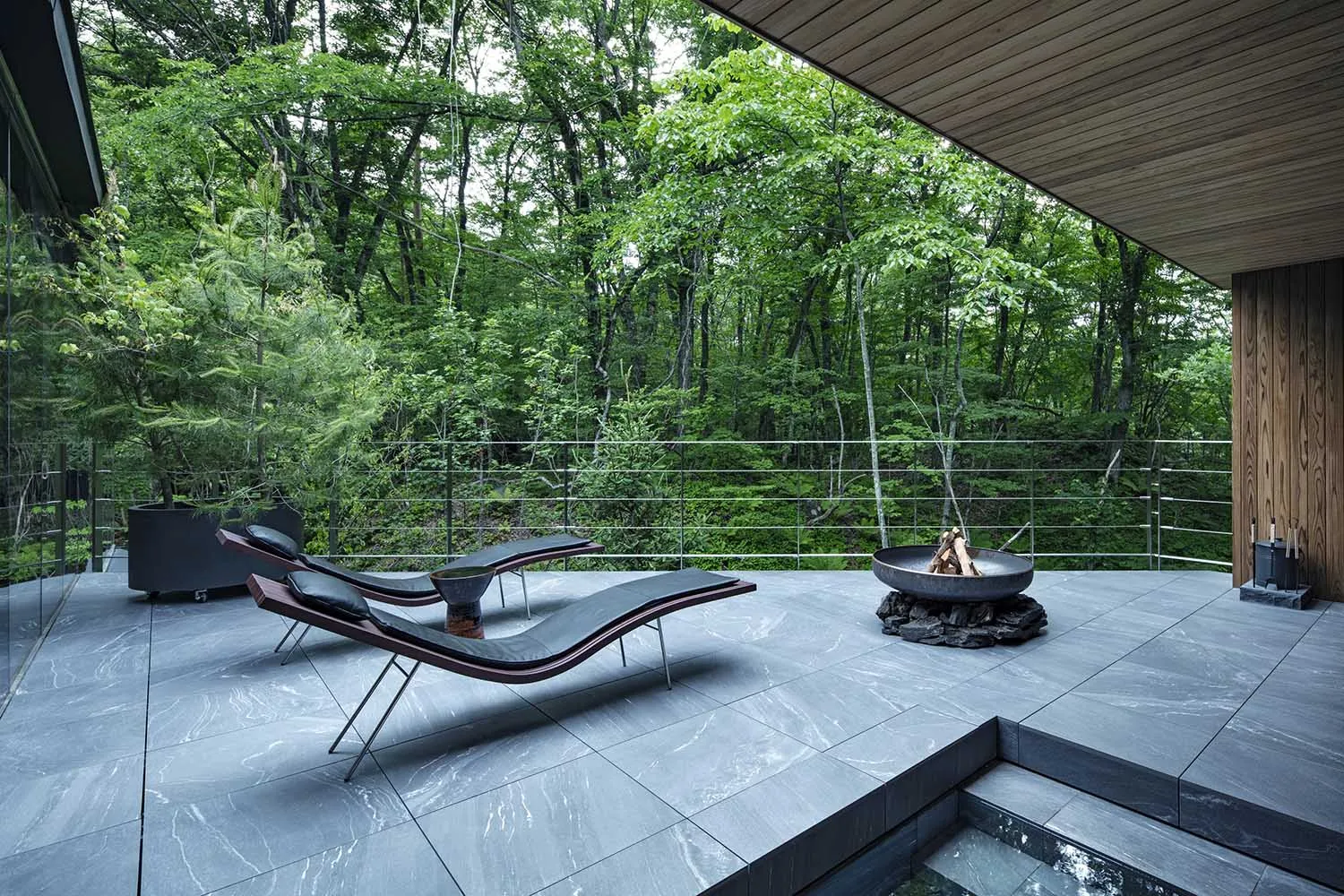 Metallic outdoor lounge area with concrete tiles, a fire pit, and two modern lounge chairs.