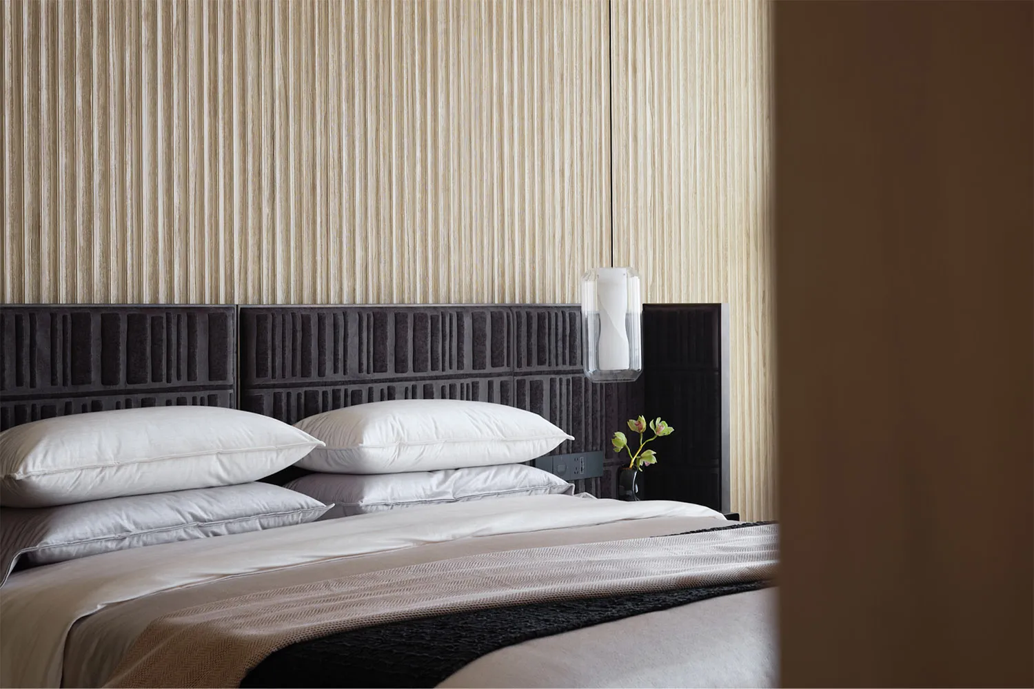 Minimalist bedroom featuring textured wallpaper, plush bedding, and a sleek black headboard.
