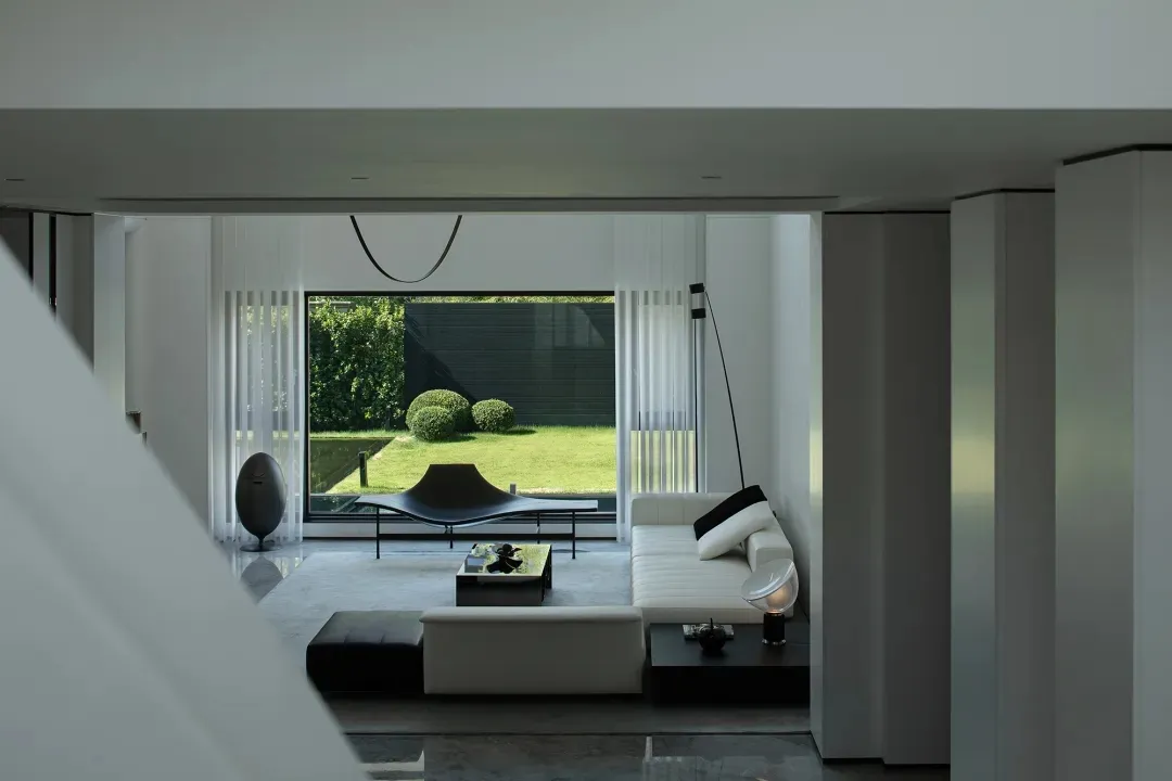 A minimalist living room with white marble accents and black furniture, featuring a large window with vertical blinds and a s