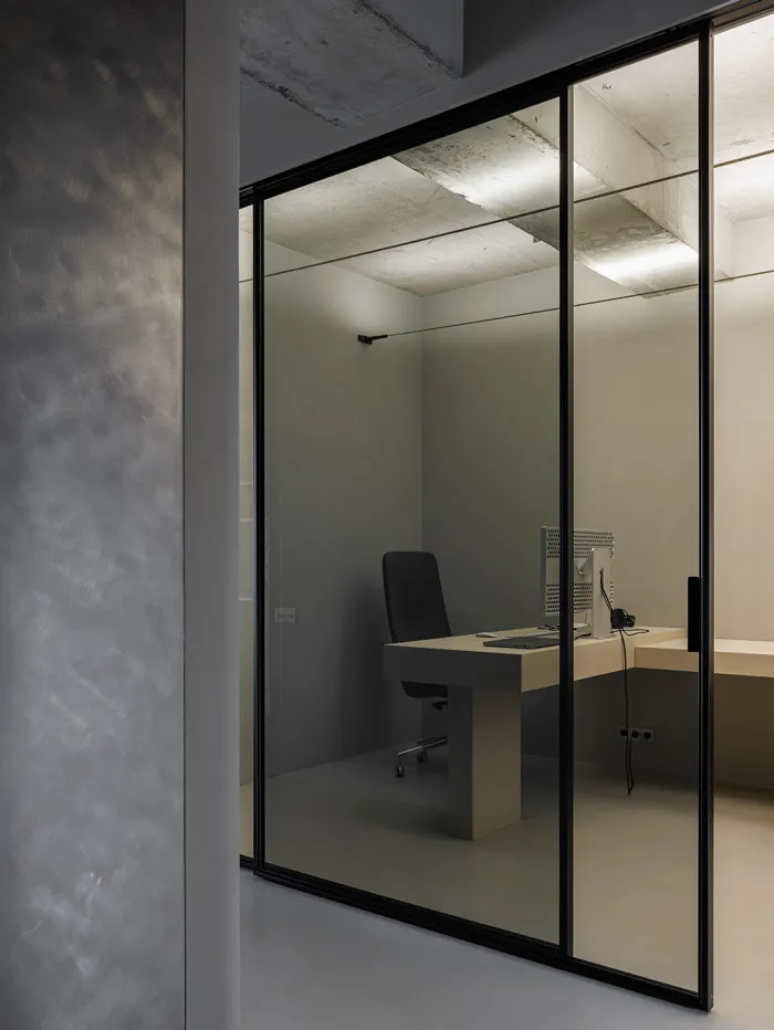 An office with a glass door, concrete walls, and metal accents.