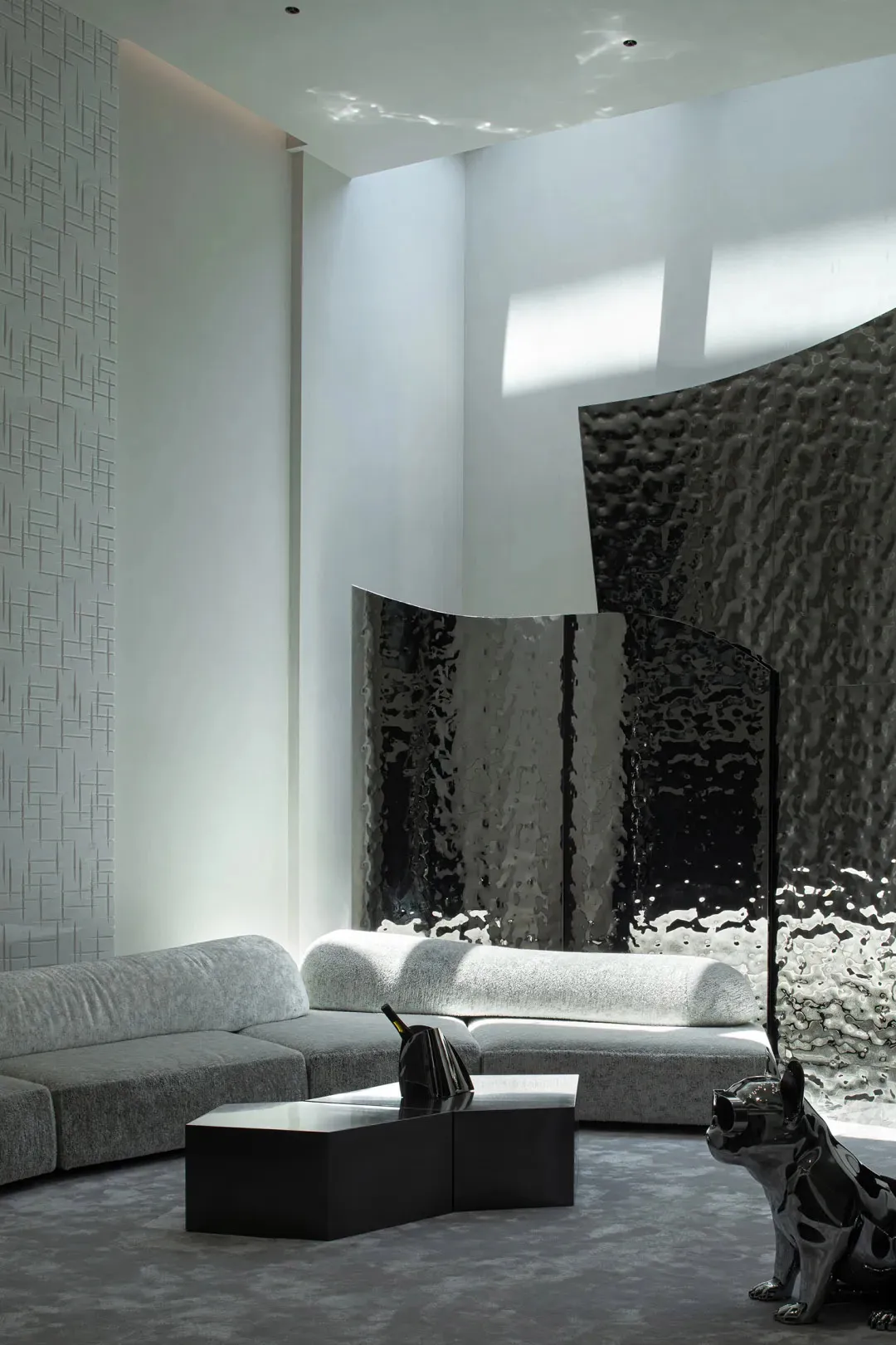 Modern interior design featuring taupe-colored fabric furniture, metallic accents, and a large window with a glass wall.