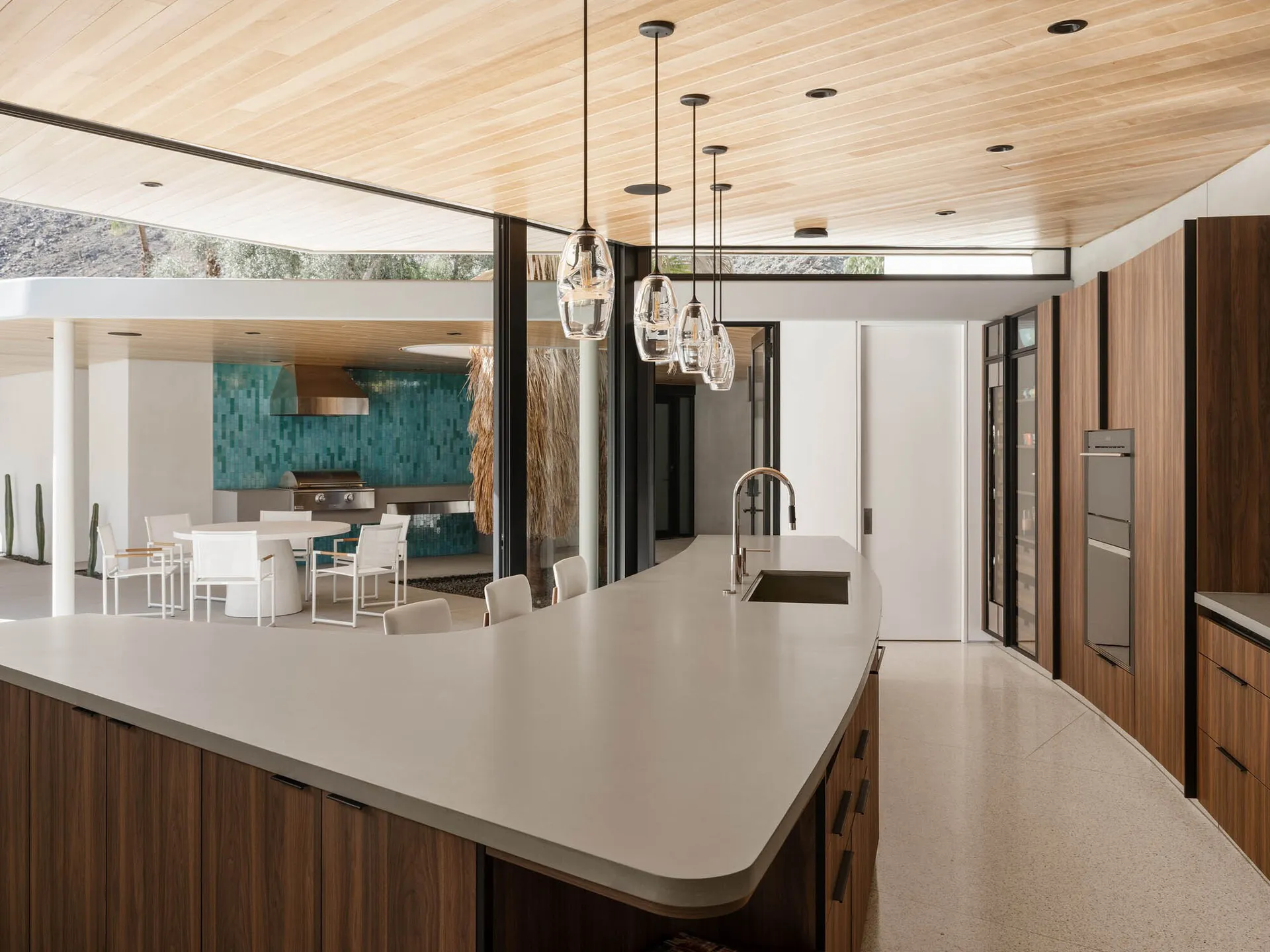 A modern kitchen featuring a concrete countertop with a curved edge, white chairs, and pendant lights.