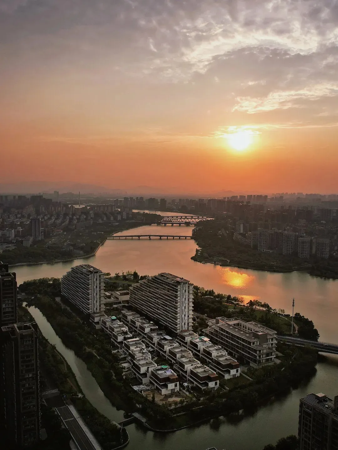 Aerial view of a cityscape featuring a river with bridges and buildings at sunset.