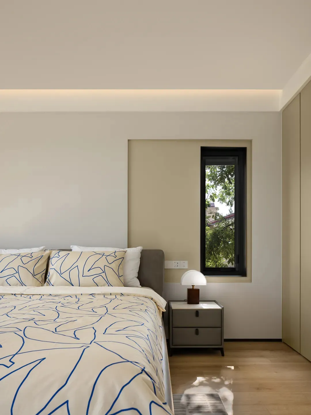 Modern minimalist bedroom featuring a bed with blue and white bedding and a side table with a lamp, set against a neutral col