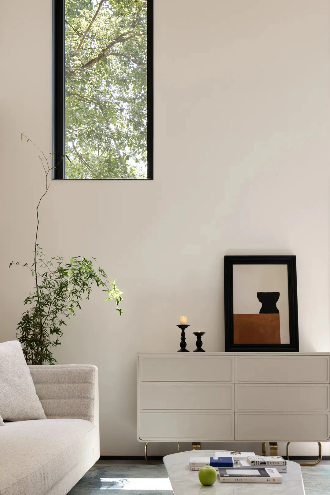 Minimalist living room featuring neutral-colored furniture and decor, with a tall window showcasing greenery outside.