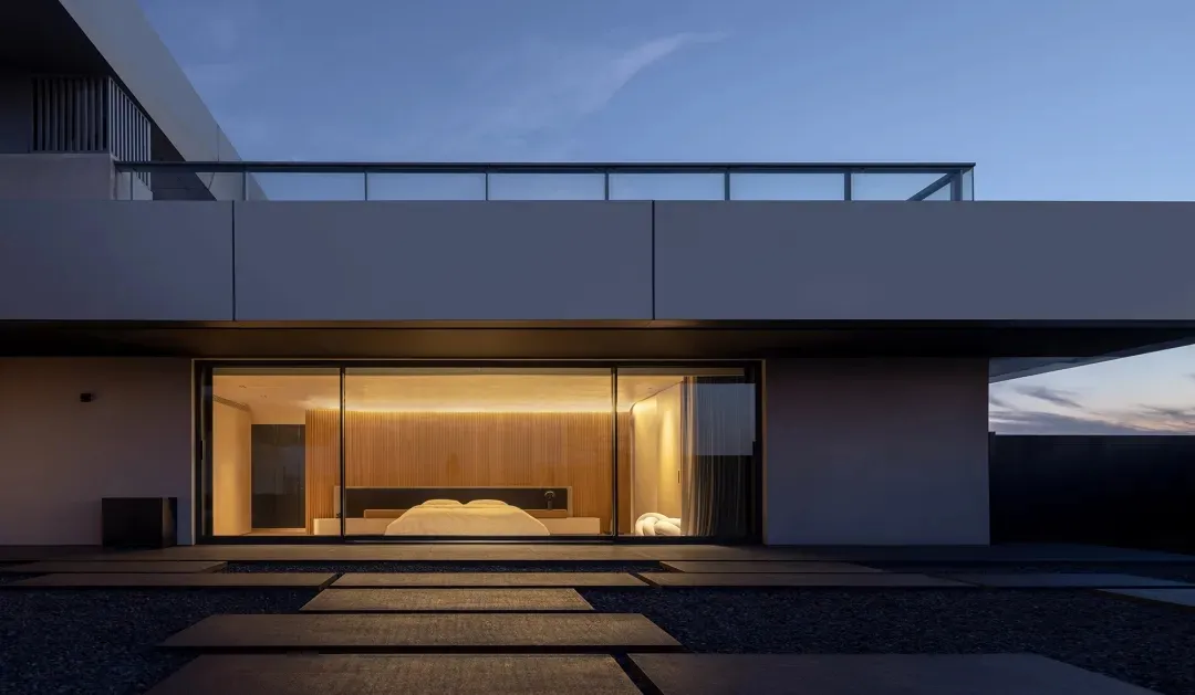A modern residential room with a glass door leading to a patio. The room features a minimalist design with a wooden accent wa