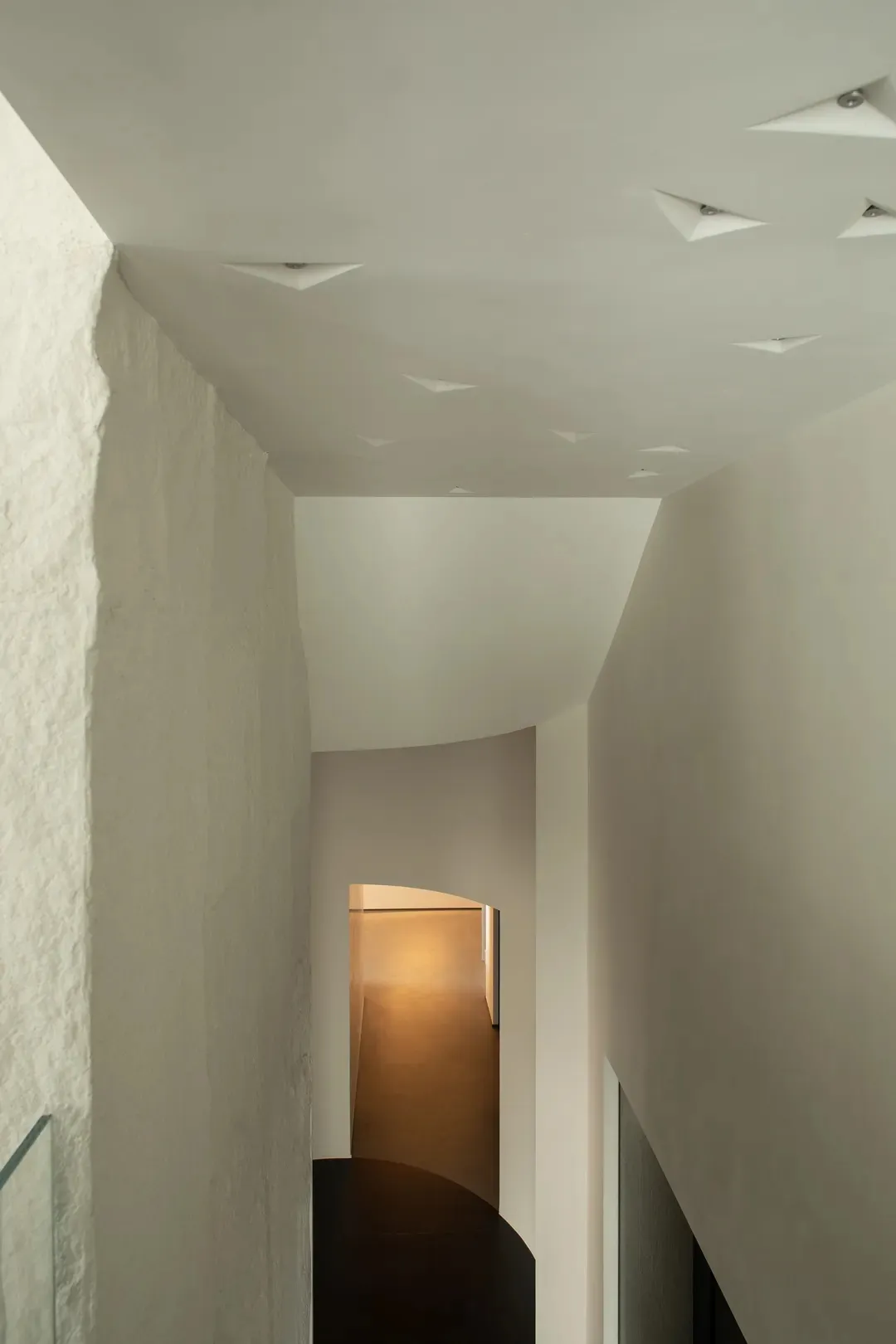 A corridor with minimalist design features, concrete walls, and geometric ceiling lights.