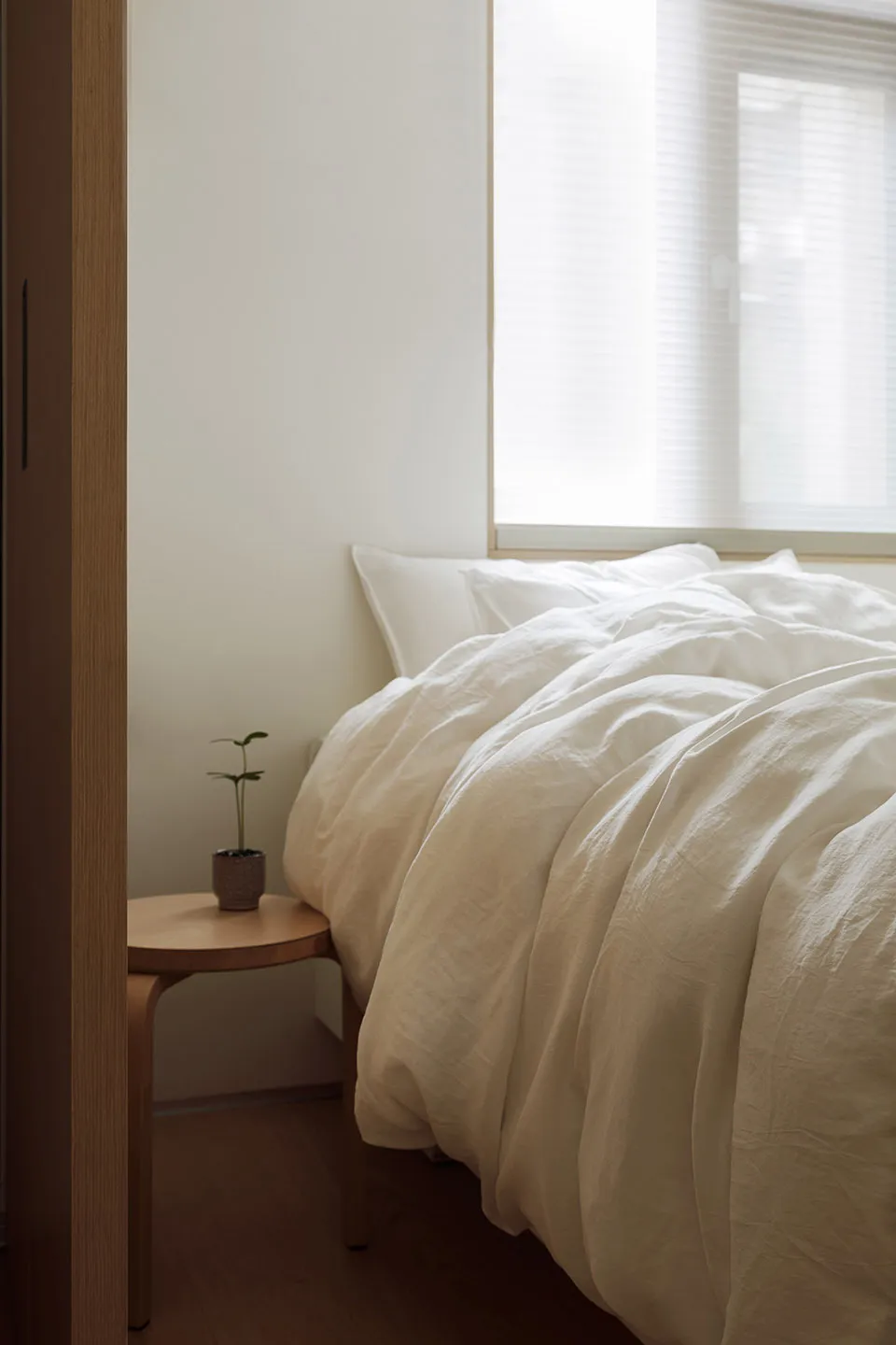 A minimalist bedroom with a bed covered in beige linen and a small wooden side table.