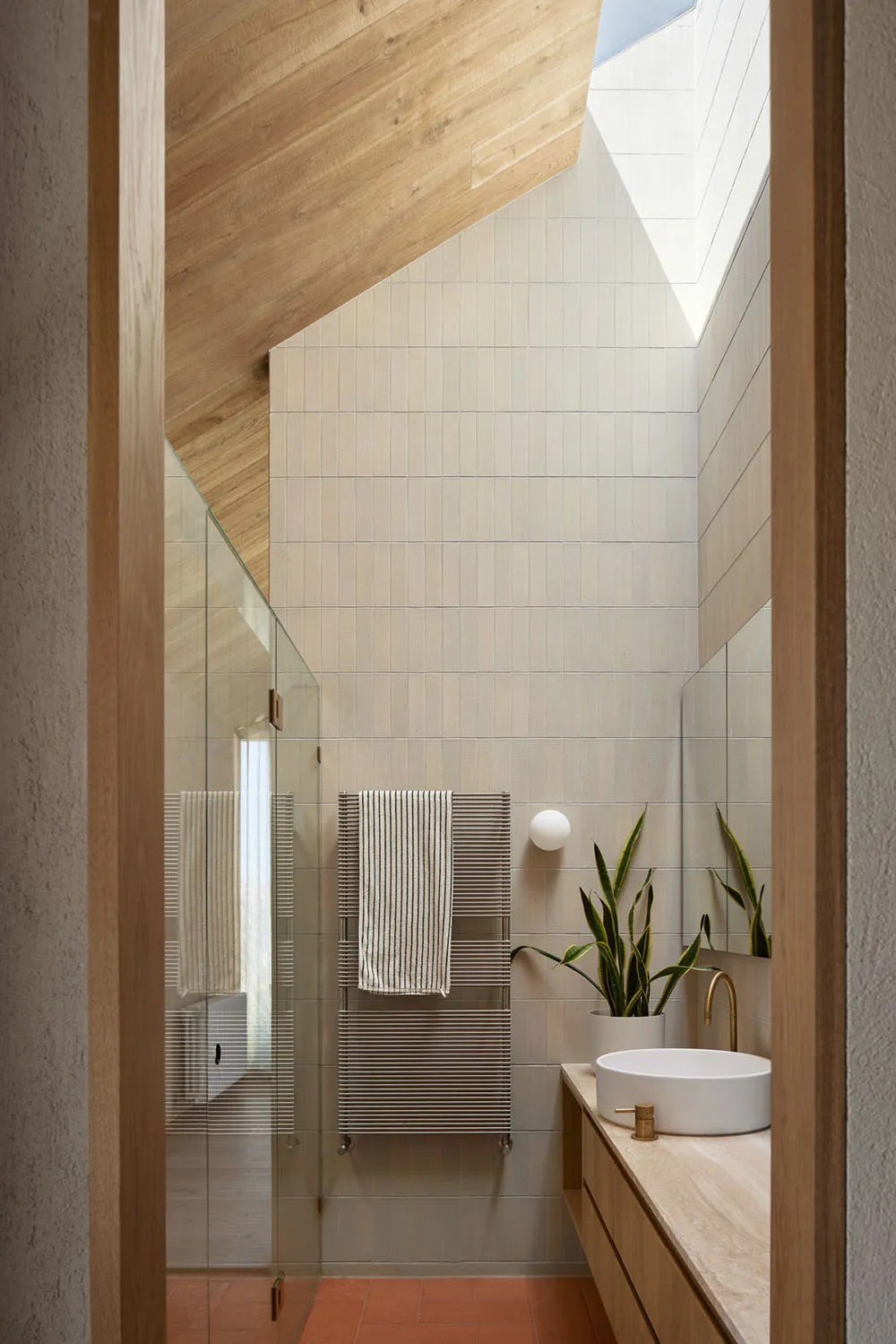 Modern bathroom with beige tiles, white sink, wooden accents, and a glass shower door.