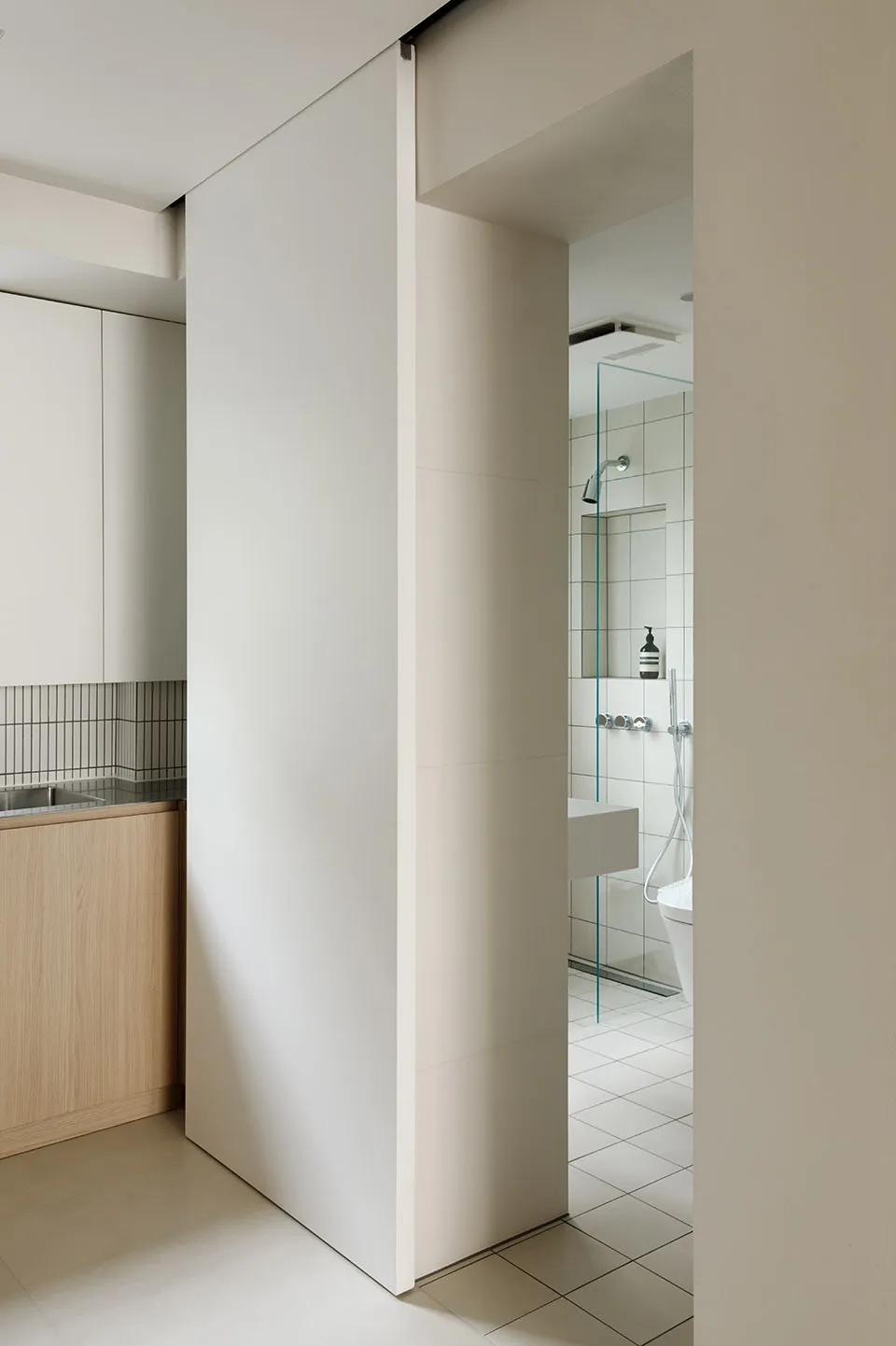 Modern bathroom with white and beige tiled walls, wooden vanity, and sliding door.