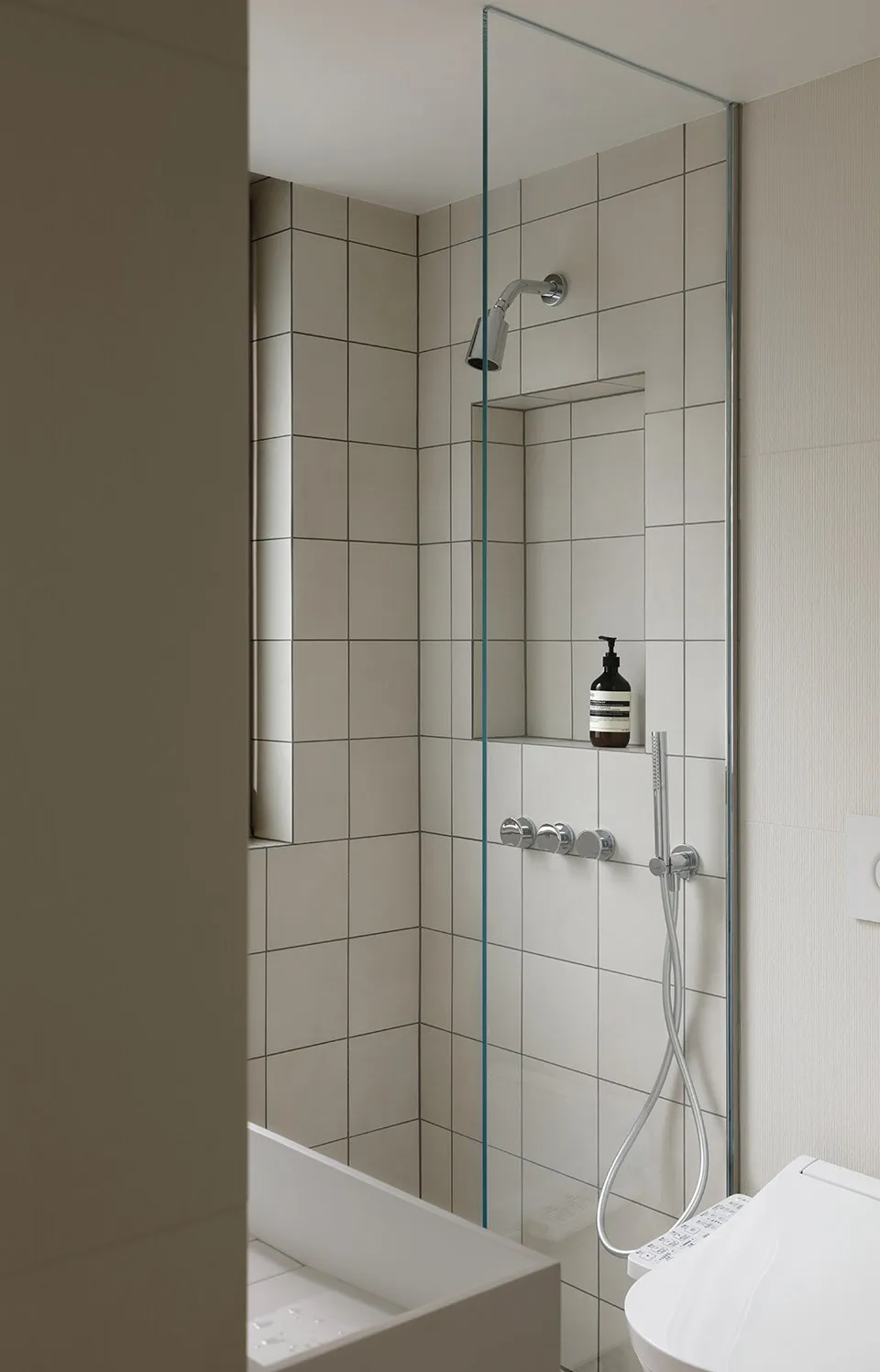 A modern bathroom featuring white tiled walls and a glass shower enclosure.
