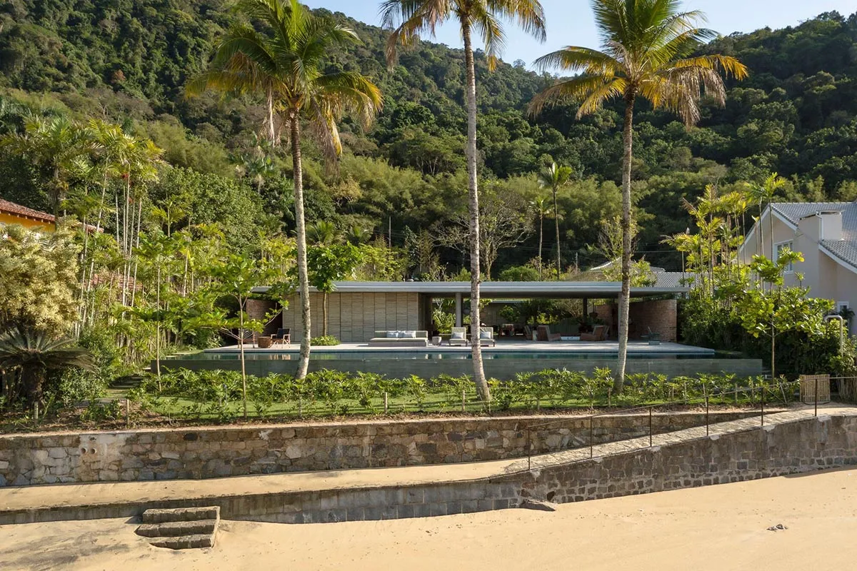 A minimalist house with concrete walls and a large glass wall, surrounded by lush greenery.