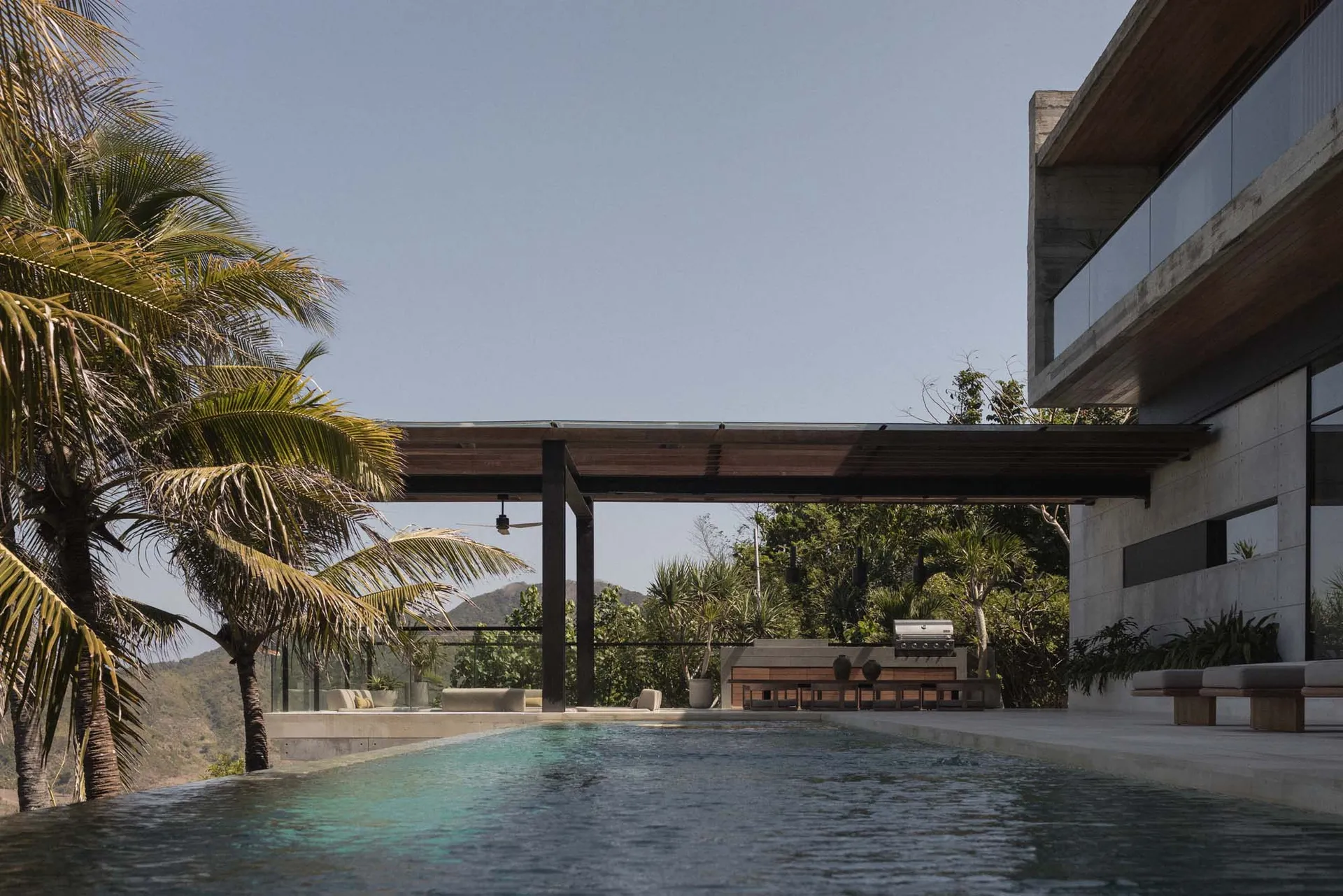 Modern, minimalist vacation home featuring concrete exterior and a large infinity pool surrounded by tropical plants and palm
