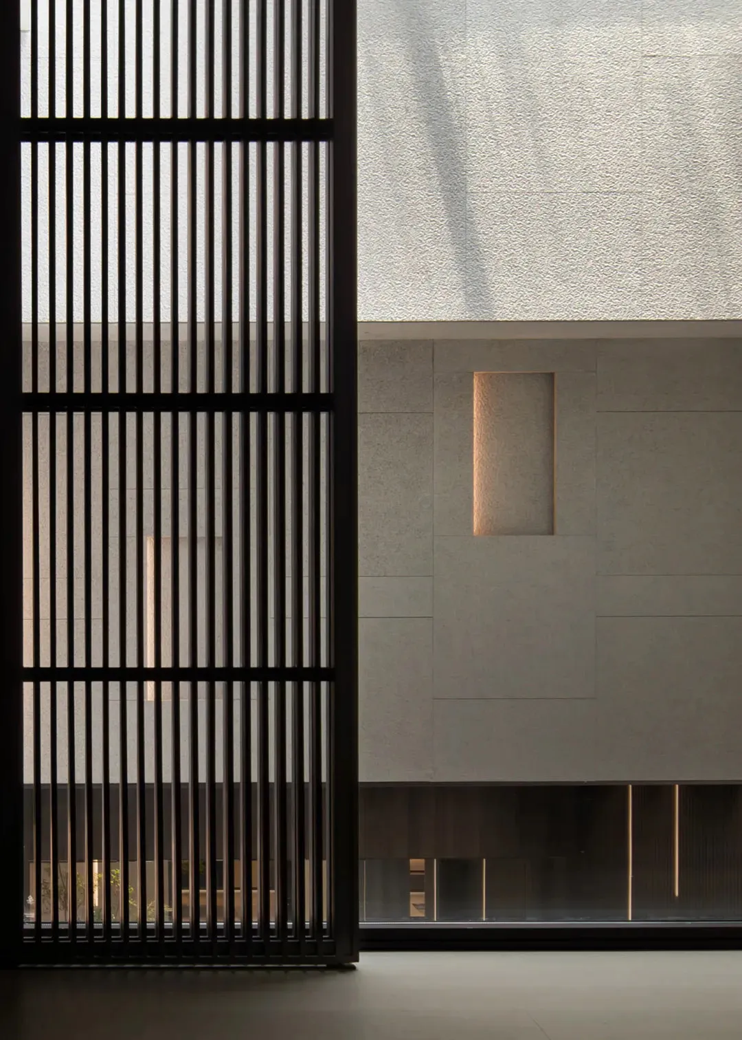 A minimalist interior with concrete walls and a large window with vertical slats.