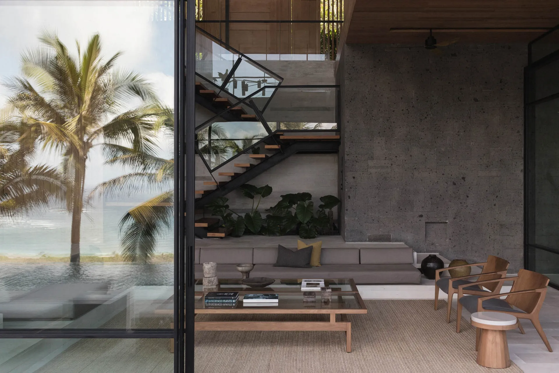 Modern living room with concrete and glass design elements, featuring a couch, chairs, and a coffee table.